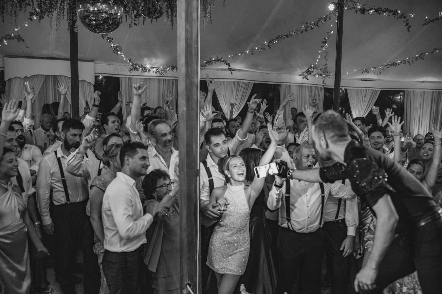 Black and white photo of wedding guests dancing and celebrating on a packed dance floor.