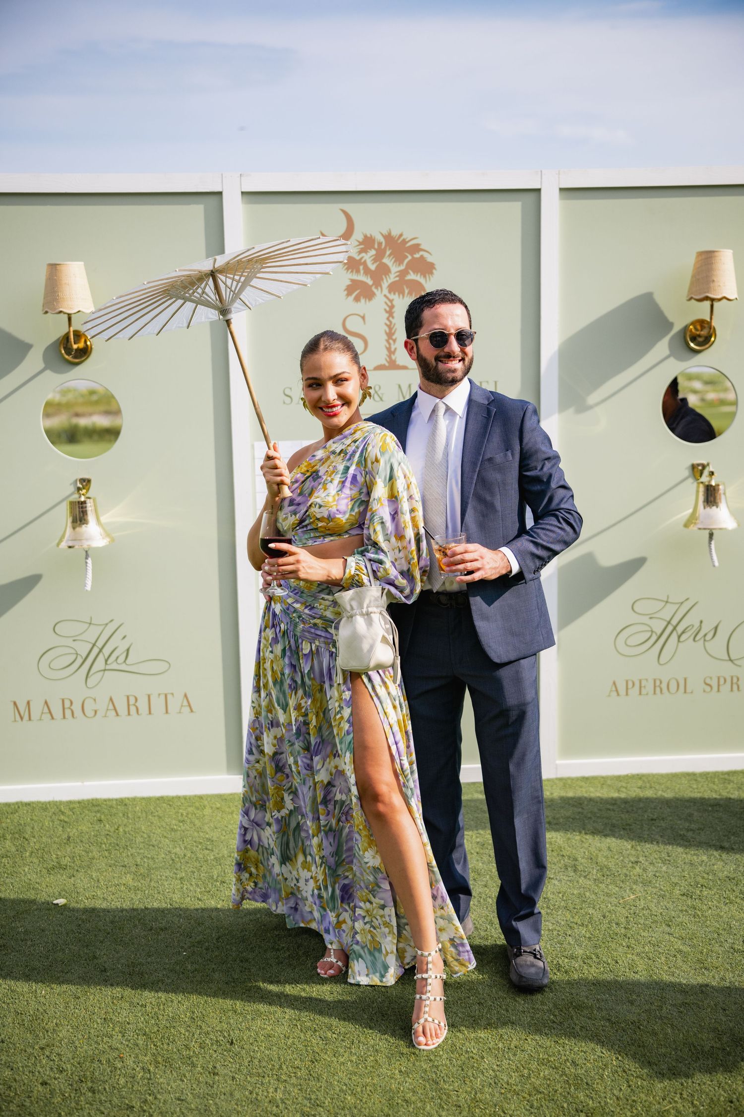 Wedding guests enjoying cocktails on a lawn with decorative wall art and margarita signage.
