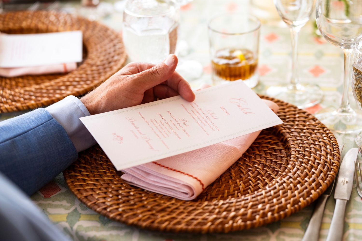 Close-up of woven rattan charger plates and pink napkins at an elegant table setting.