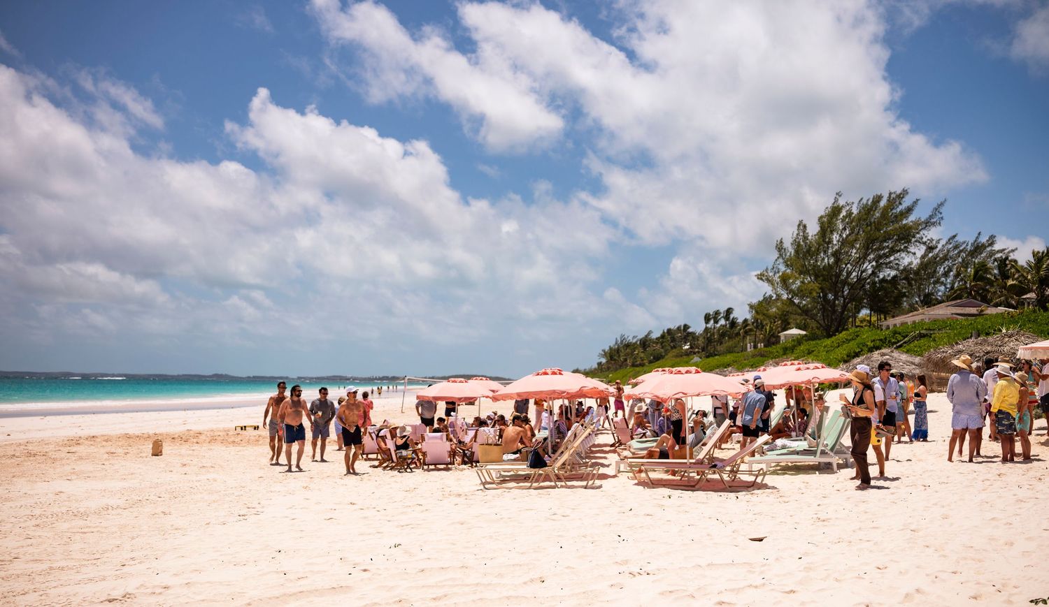 Panoramic view of a pristine white sand beach with turquoise waters and scattered beachgoers under blue skies.