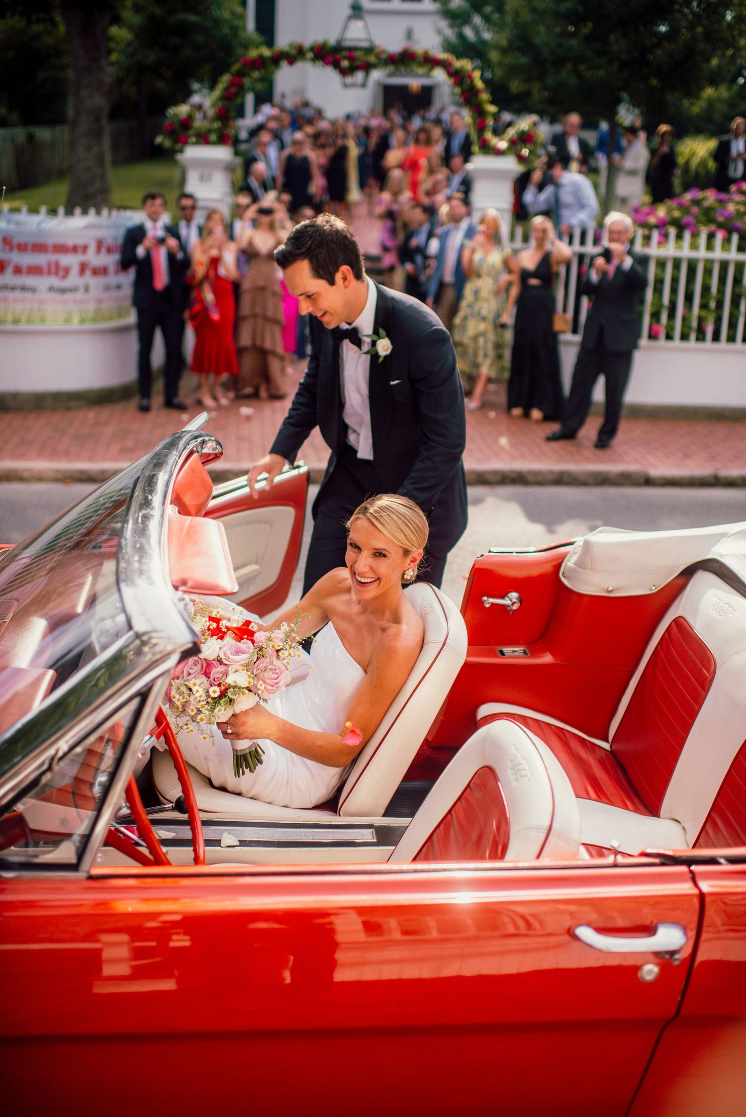 Happy couple enjoying moments in a classic red convertible car during their wedding celebration.