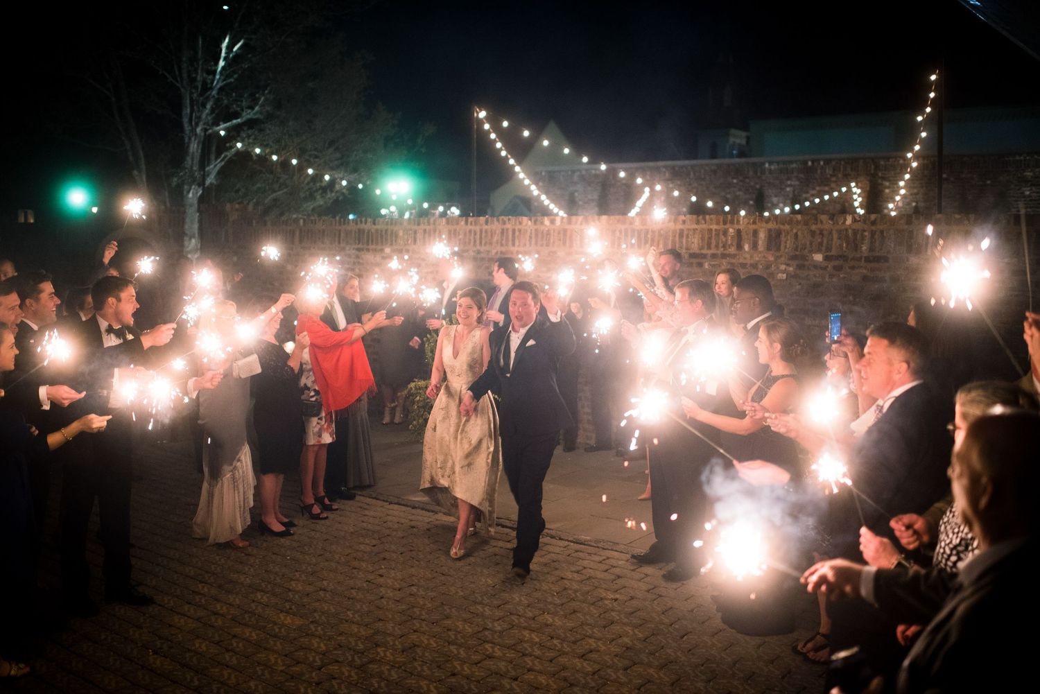 Wedding guests create a magical sparkler tunnel exit for the newlyweds during an outdoor nighttime celebration.