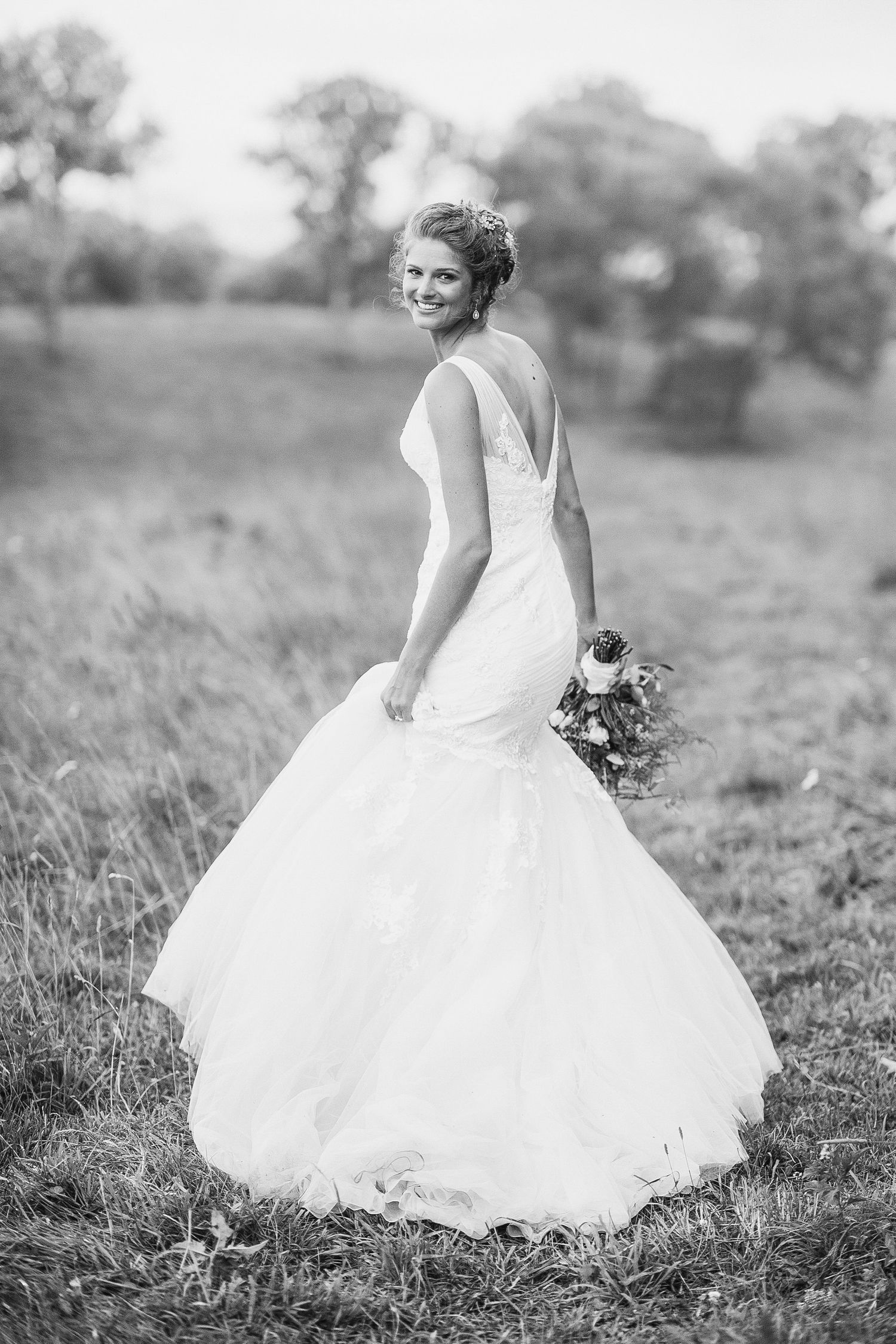 Bride twirling in a flowing white wedding gown in a sunlit meadow.