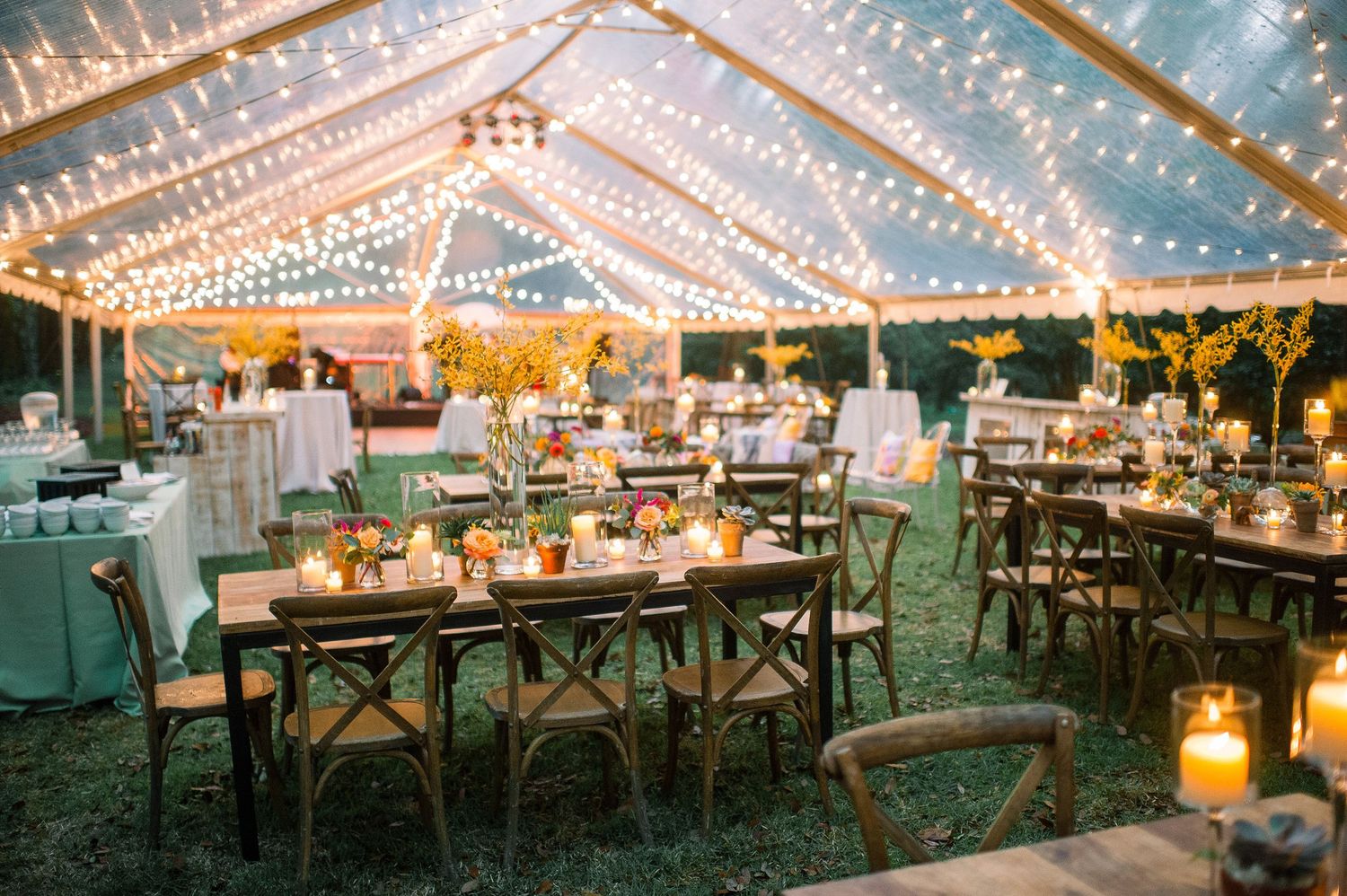 Wedding reception tables set under a clear tent with twinkling string lights creating a magical evening ambiance.