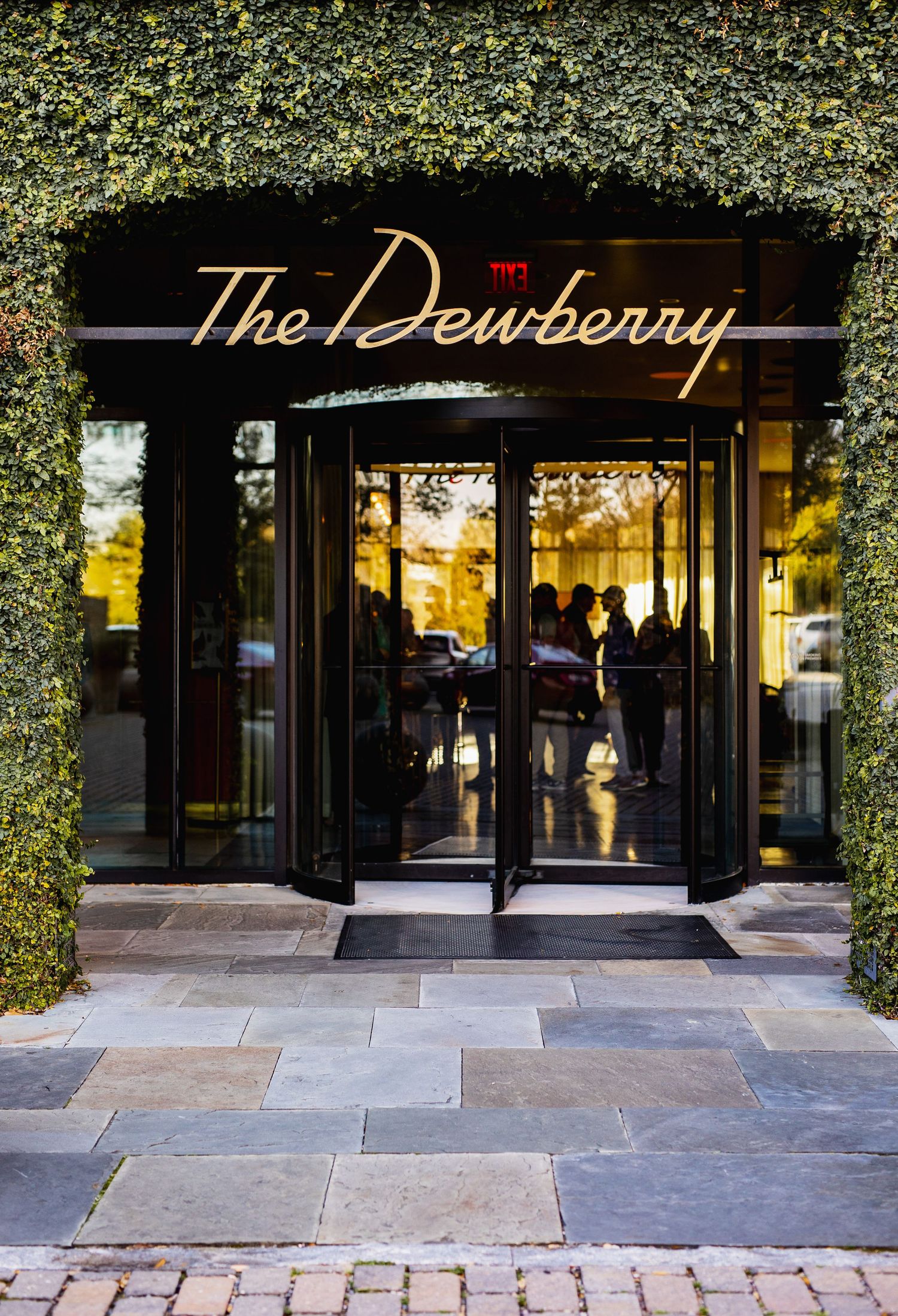 Elegant storefront entrance of The Dewberry hotel with glass doors and stone facade at golden hour.