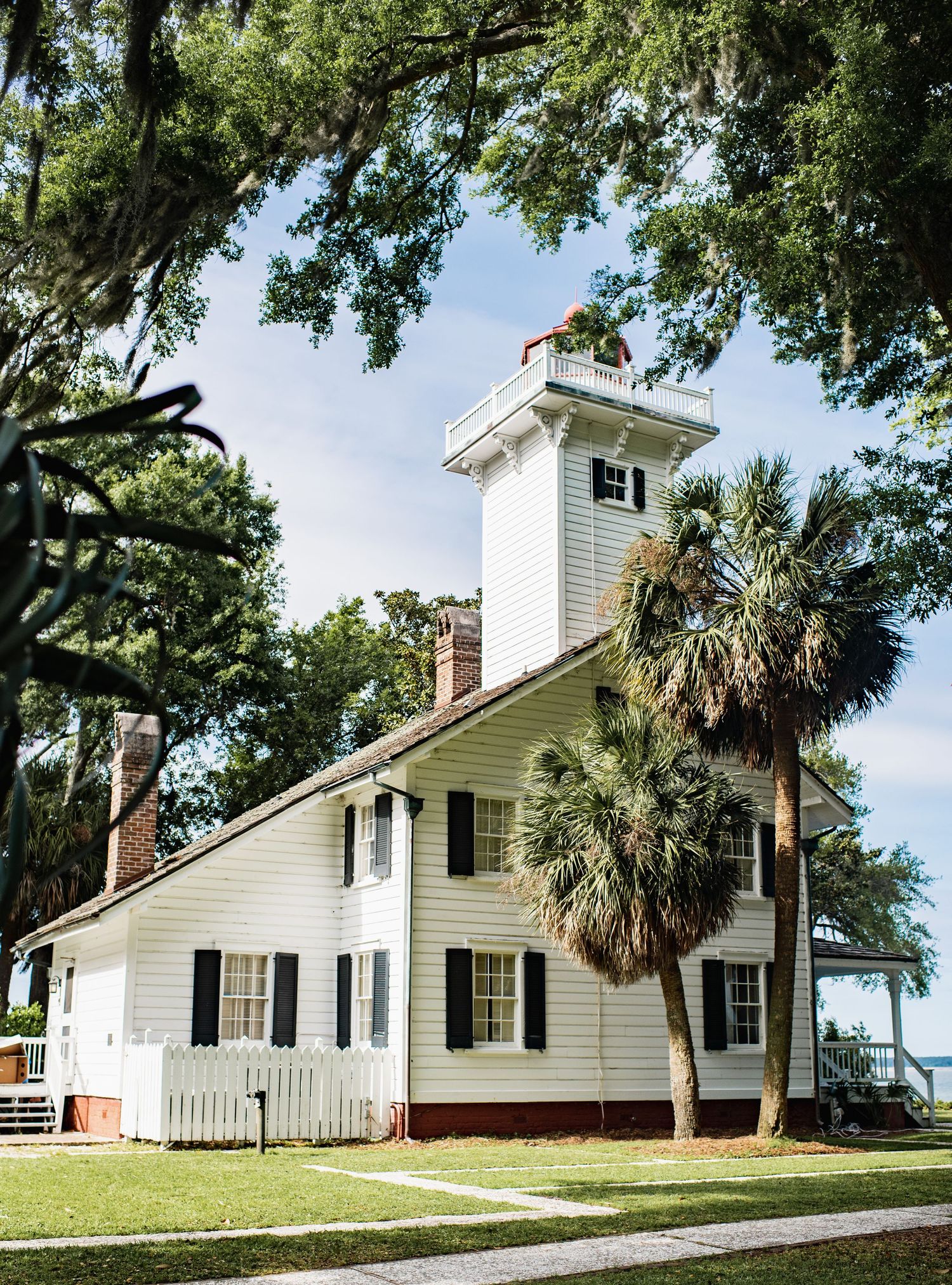 Historic white church building with tall steeple and palm trees shown from multiple angles on a grassy hill.