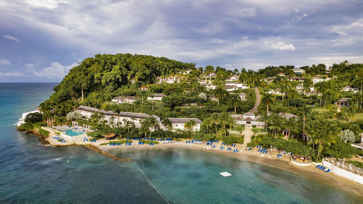 Aerial view of a tropical beach resort nestled on a lush green hillside overlooking turquoise Caribbean waters.