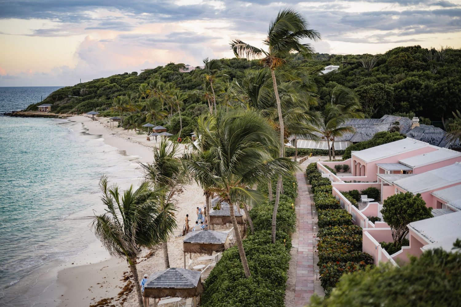 Aerial view of luxury beachfront villas with palm trees along a pristine Caribbean coastline at sunset.