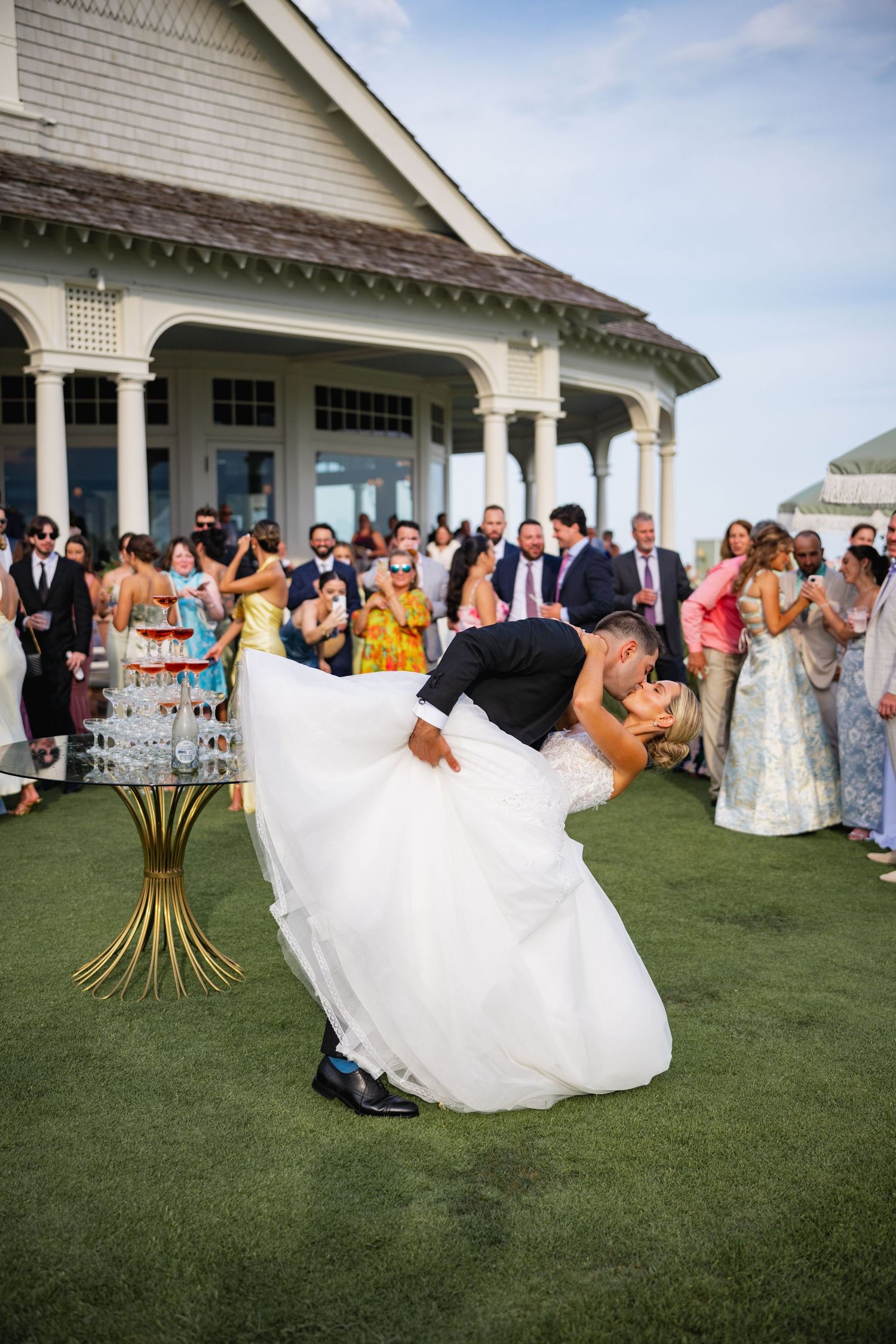 A romantic dip during a wedding dance on a manicured lawn with guests watching in the background.