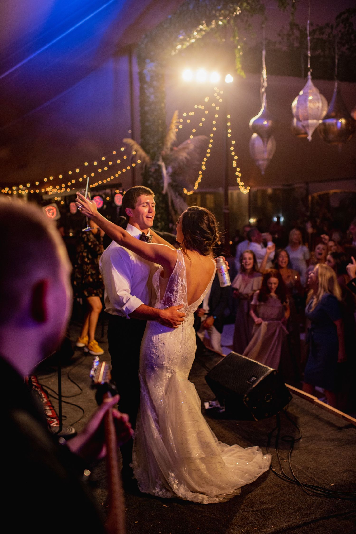 Newlyweds share their first dance at an evening wedding reception under twinkling string lights.