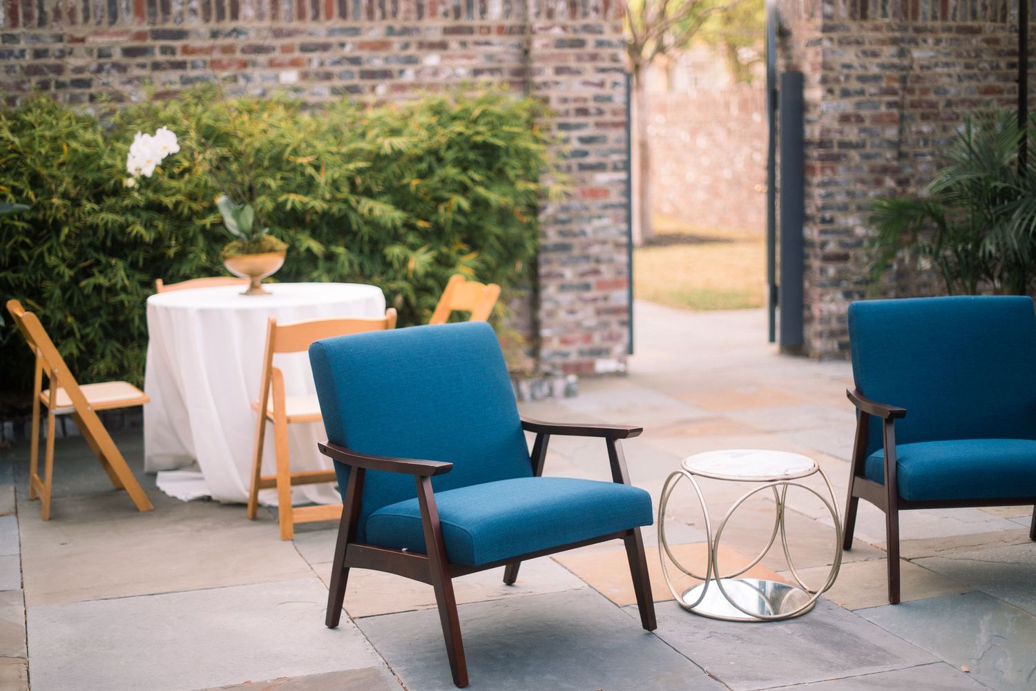Vintage mid-century modern blue velvet chairs arranged in an elegant outdoor venue setting with brick walls.