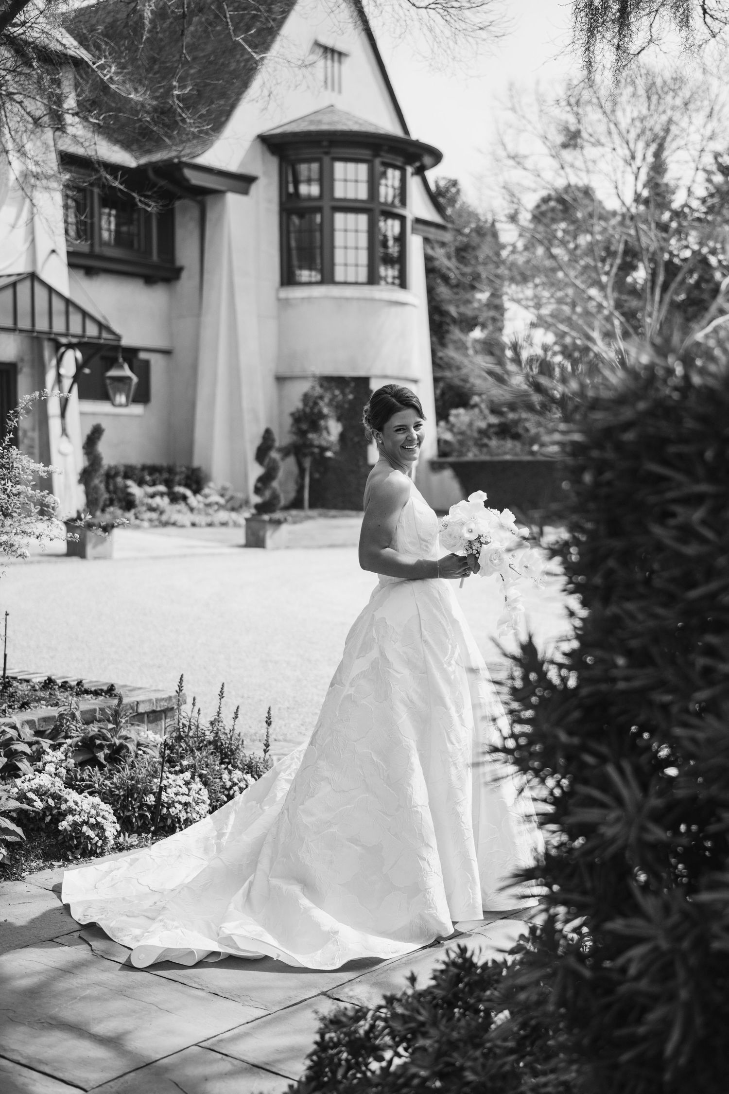 Black and white wedding photo showing a bride in a flowing white gown standing in front of a charming Tudor-style house.