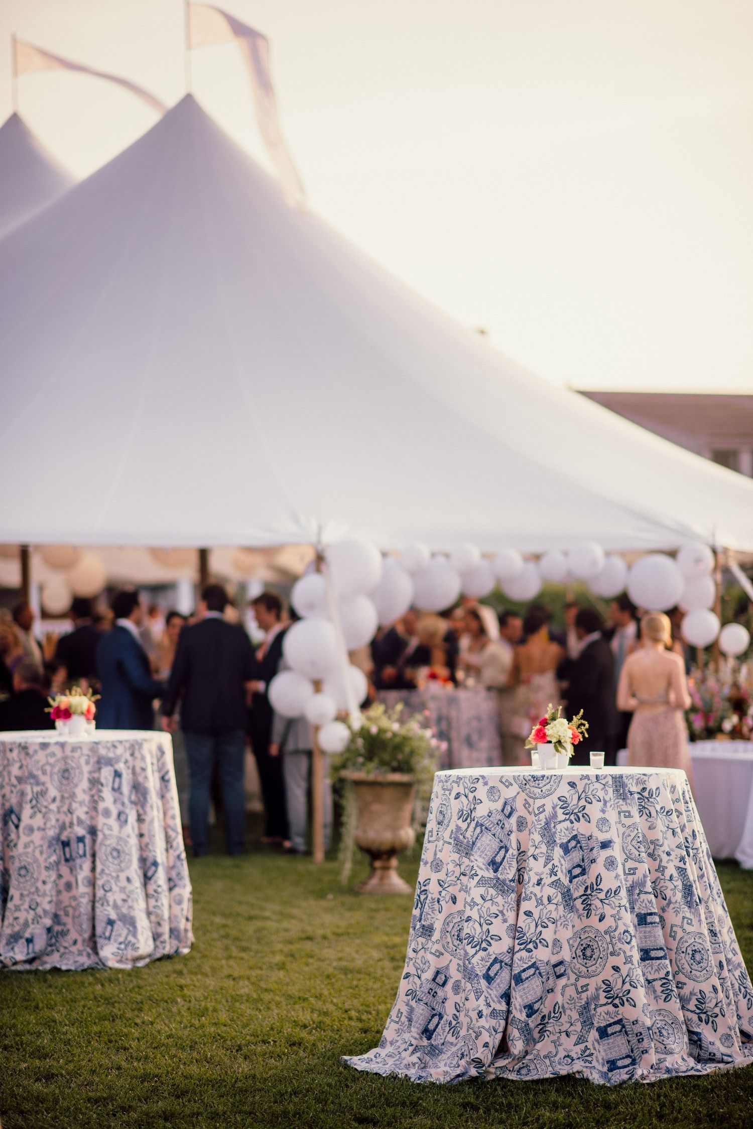 Elegant outdoor wedding reception setup with white tents and blue patterned tablecloths on grass.