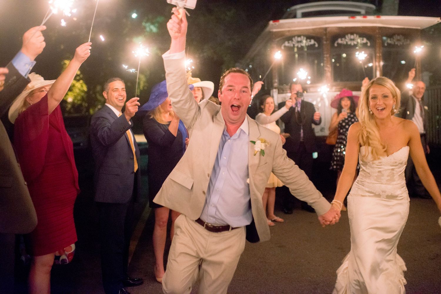 Wedding guests hold sparklers during a nighttime celebration as newlyweds walk through.