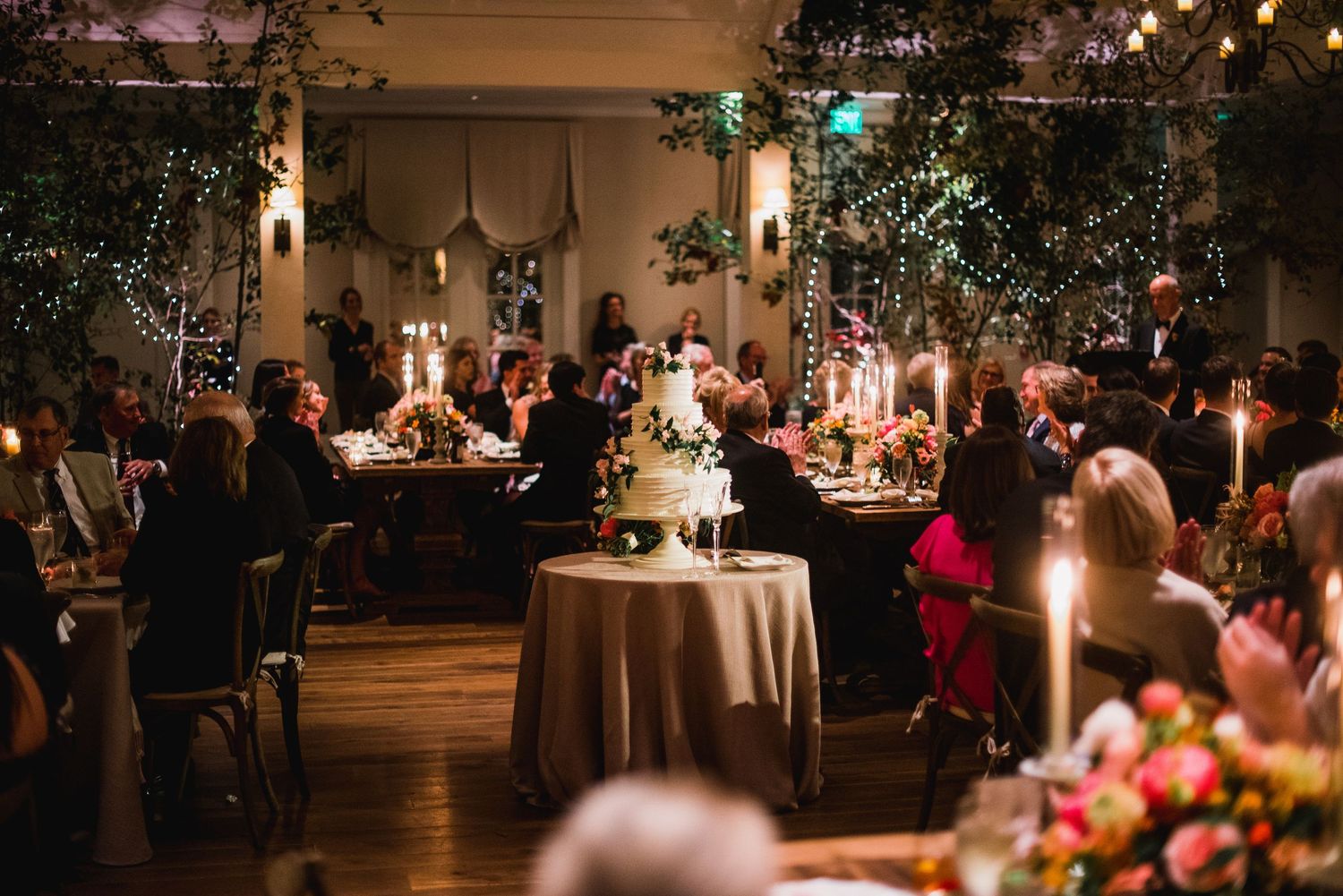 Elegant wedding reception in a dimly lit room with candlelit tables, floral centerpieces and decorative trees.