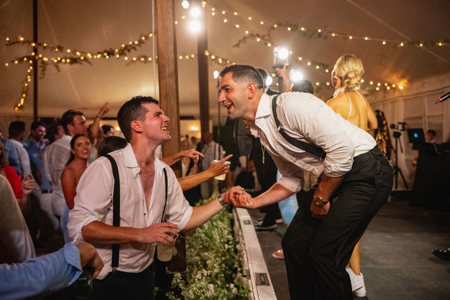 Evening wedding reception with guests dancing under romantic string light decorations.