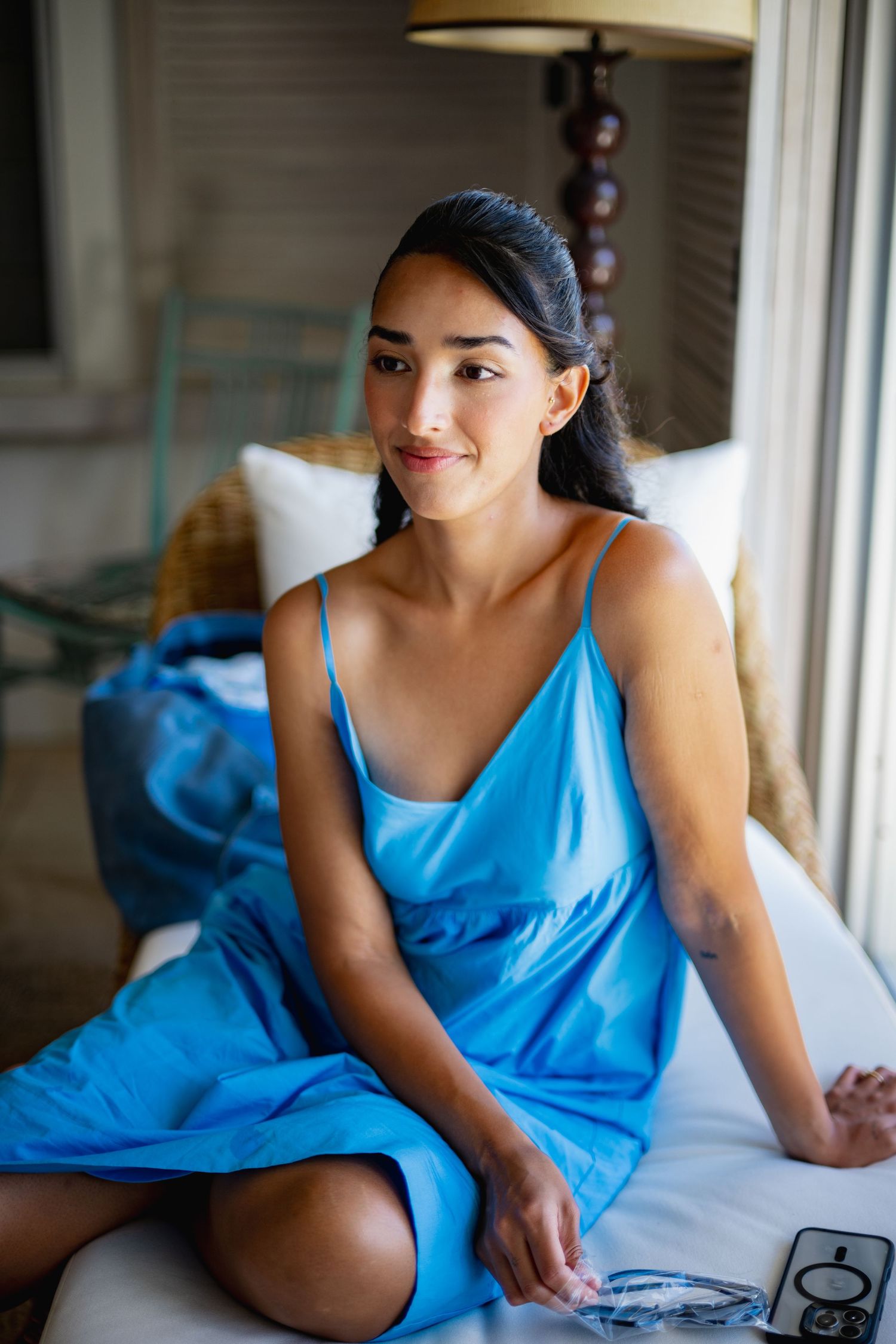 Woman in bright blue dress lounges casually indoors by a window in a series of candid poses.