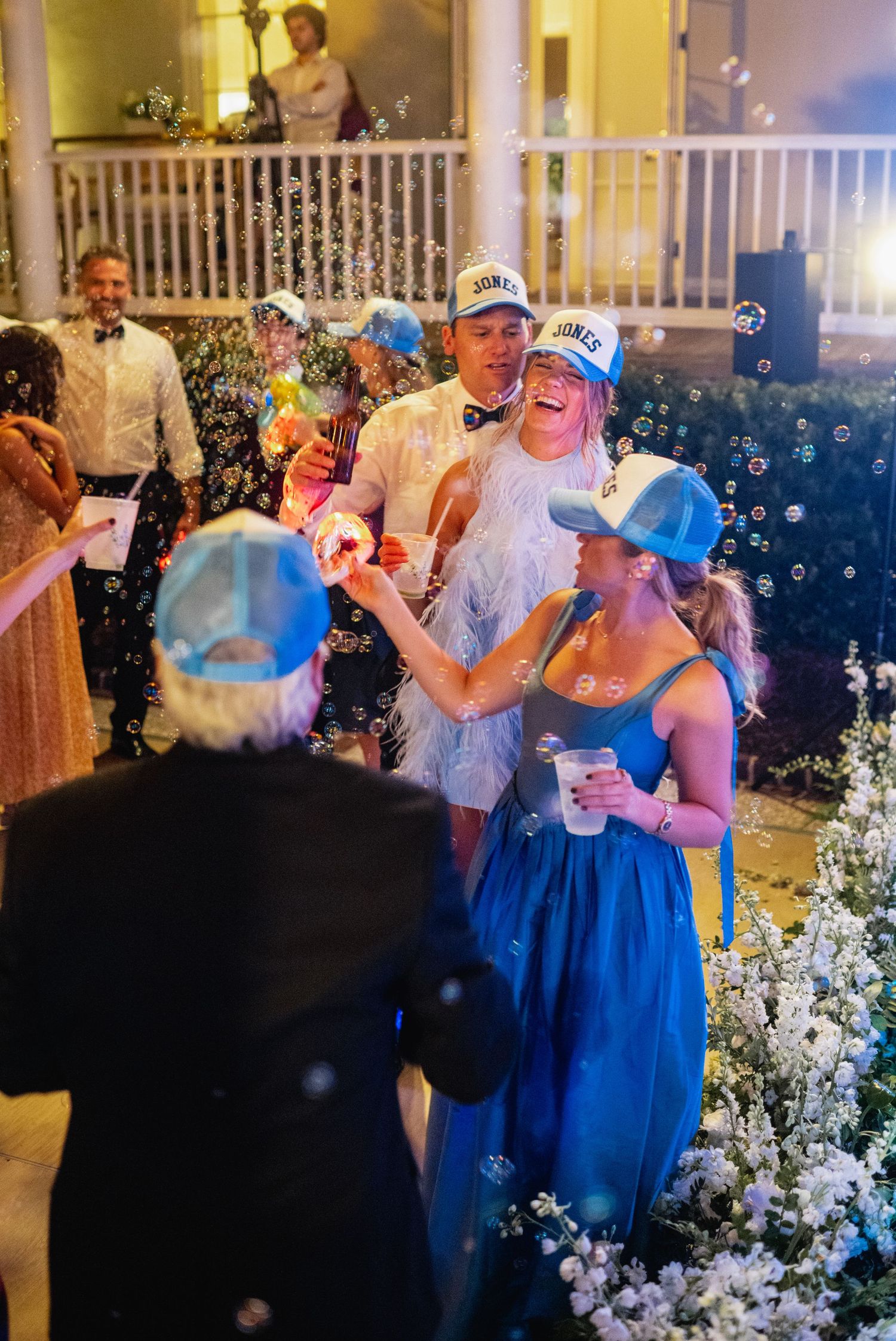 Wedding guests dance and celebrate at a reception with bubbles floating through the air and blue dresses.