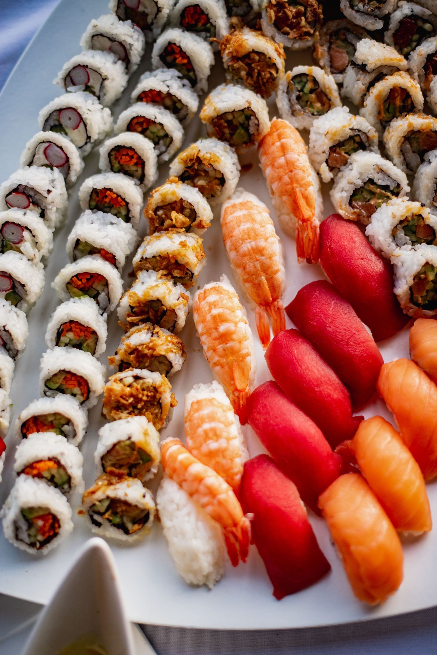 A platter of assorted sushi rolls and nigiri including spicy tuna rolls, salmon nigiri, and tuna nigiri arranged in neat rows.