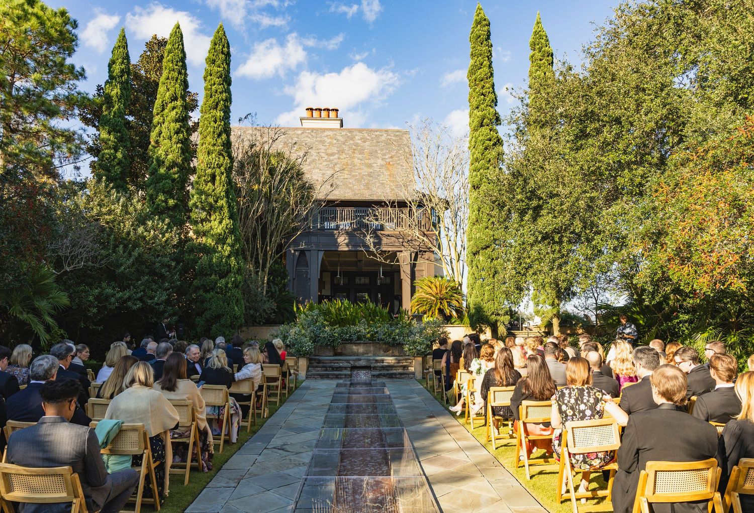 Outdoor dining patio with wooden chairs and tables surrounded by lush trees on a sunny afternoon.