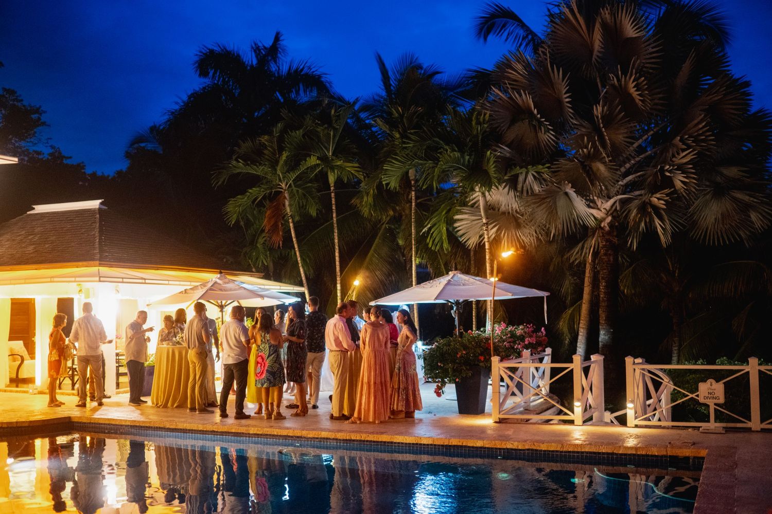Palm trees silhouetted against a deep blue twilight sky create a tropical ambiance at an outdoor evening venue.