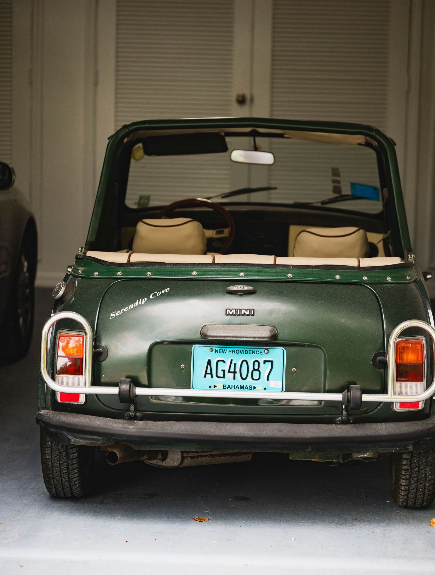 Rear view of a vintage green Mini Cooper convertible parked in a garage with tan leather seats and license plate visible.