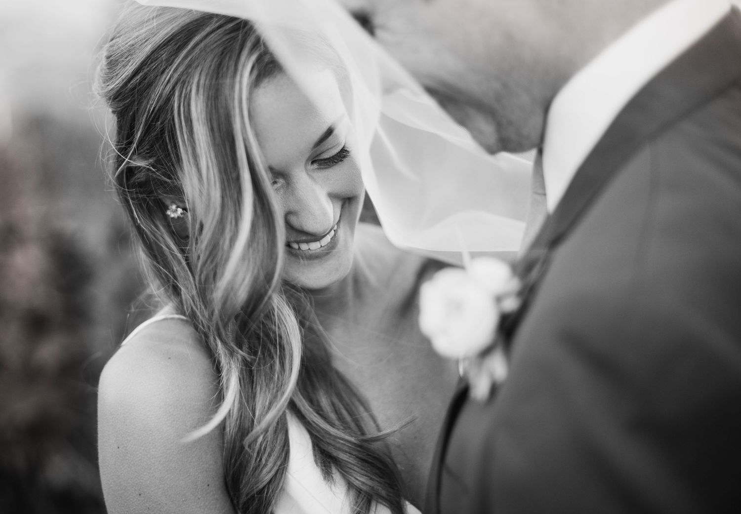 Black and white candid wedding photo showing a joyful moment between a bride and groom during their ceremony.