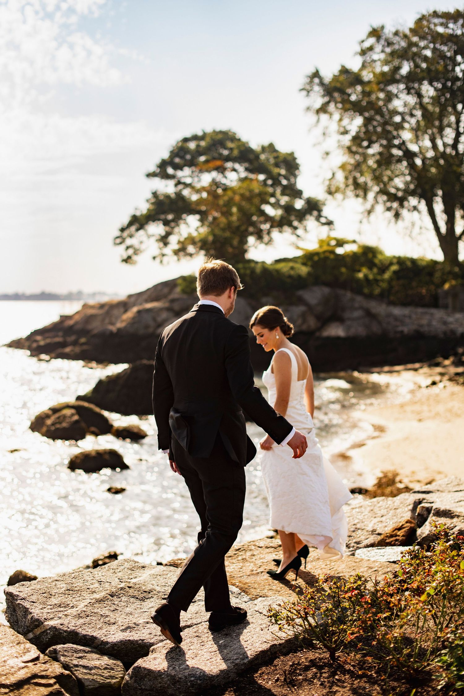 Wedding couple exploring rocky beach shoreline at sunset.