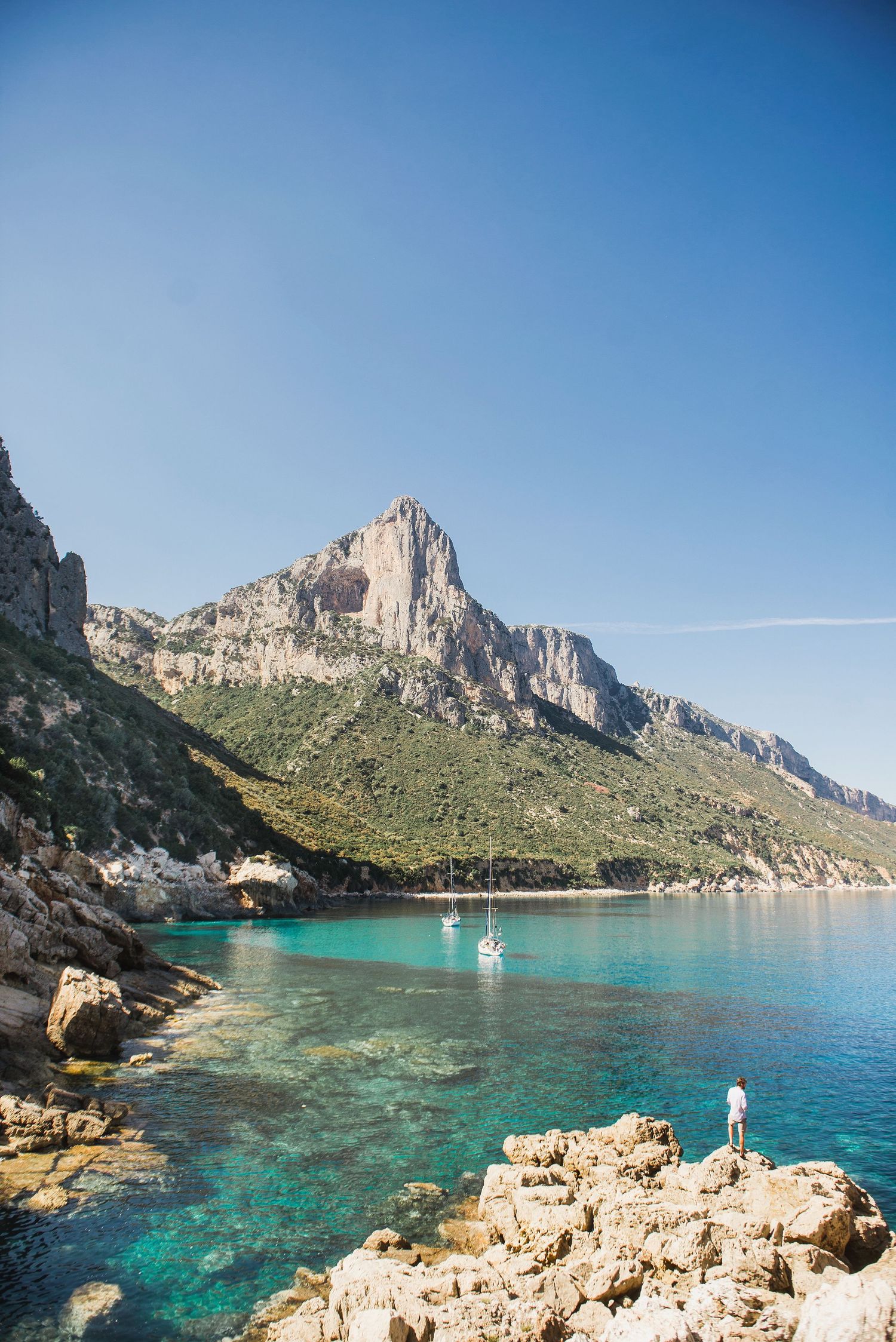 Stunning Mediterranean coastline with turquoise waters and dramatic rocky cliffs against blue sky.
