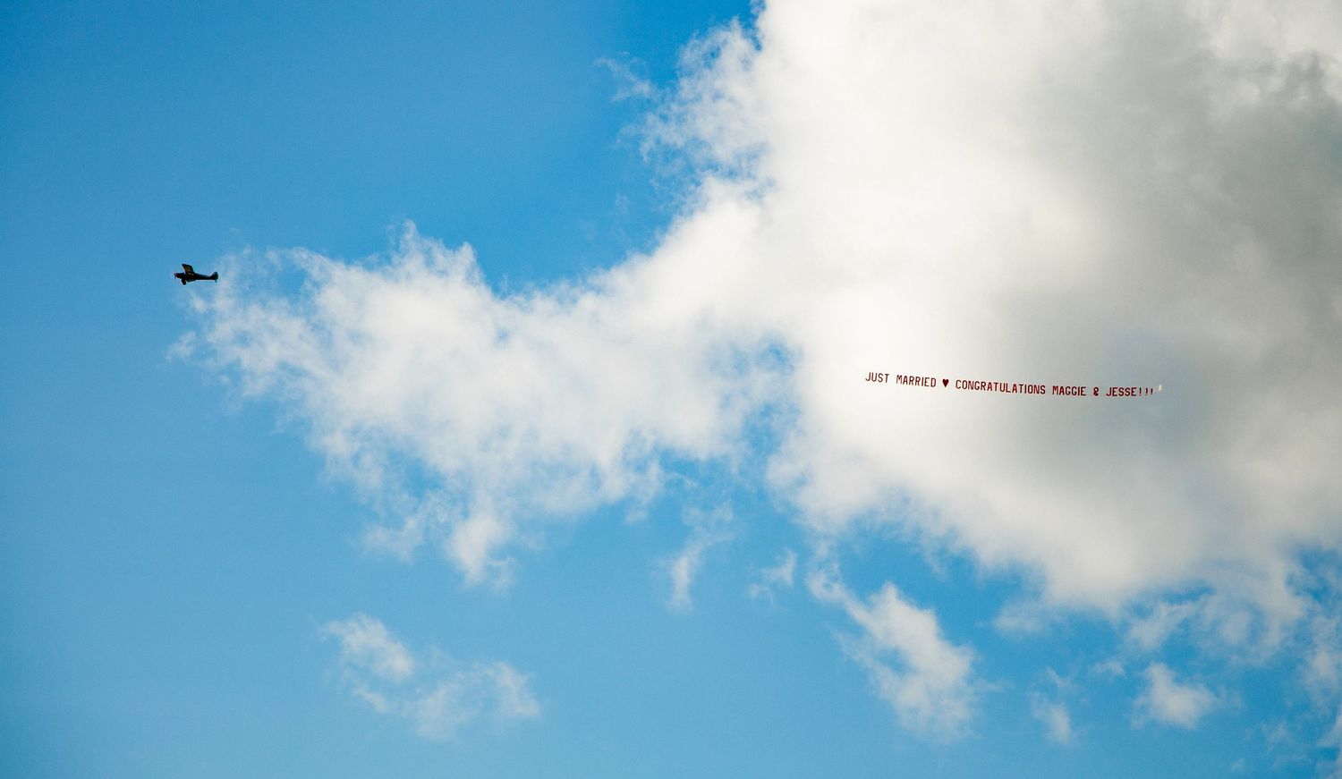 Helicopter flying through blue sky pulling an advertising banner against white clouds.