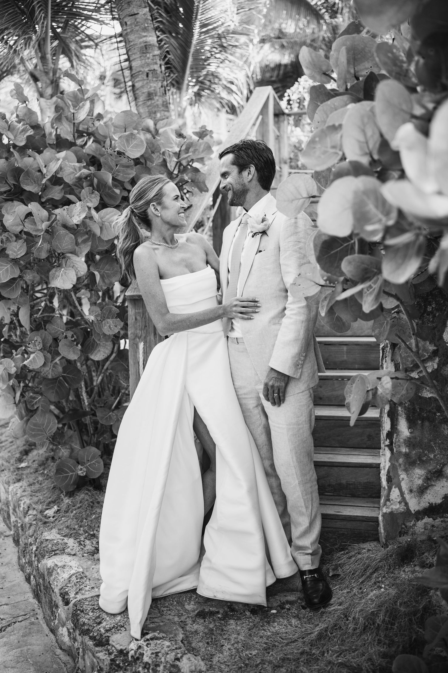 Black and white wedding photo of couple embracing on tropical garden stairway.