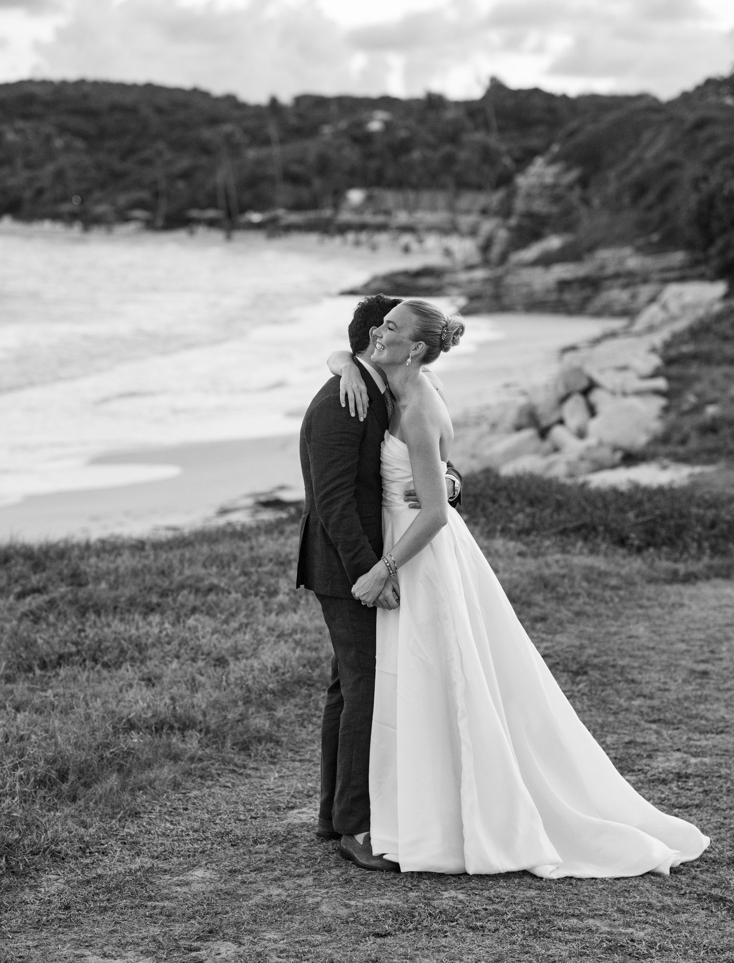 Black and white wedding portrait on a scenic coastal hillside.