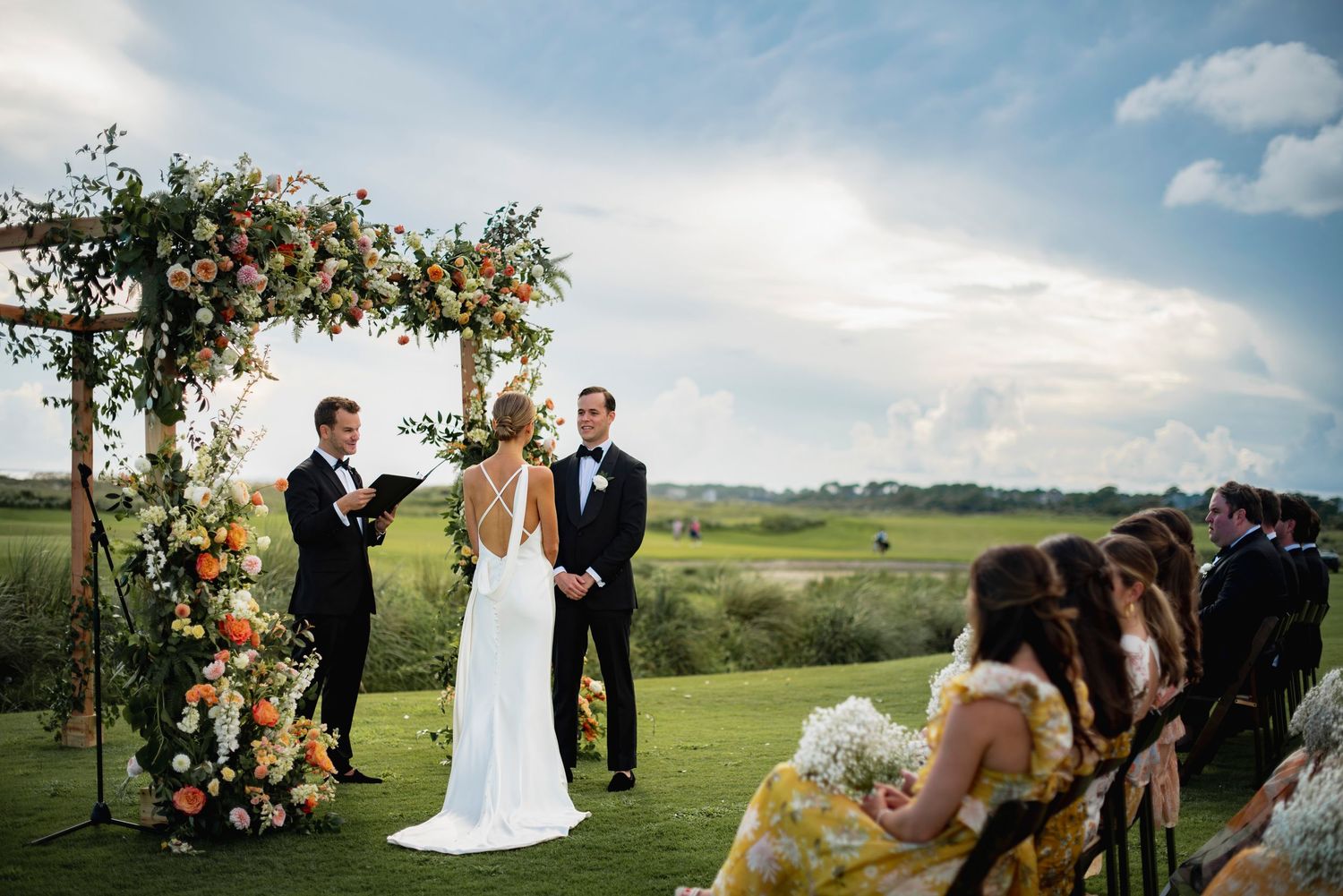 A beautiful outdoor wedding ceremony takes place on a hilltop with rolling countryside views in the background.
