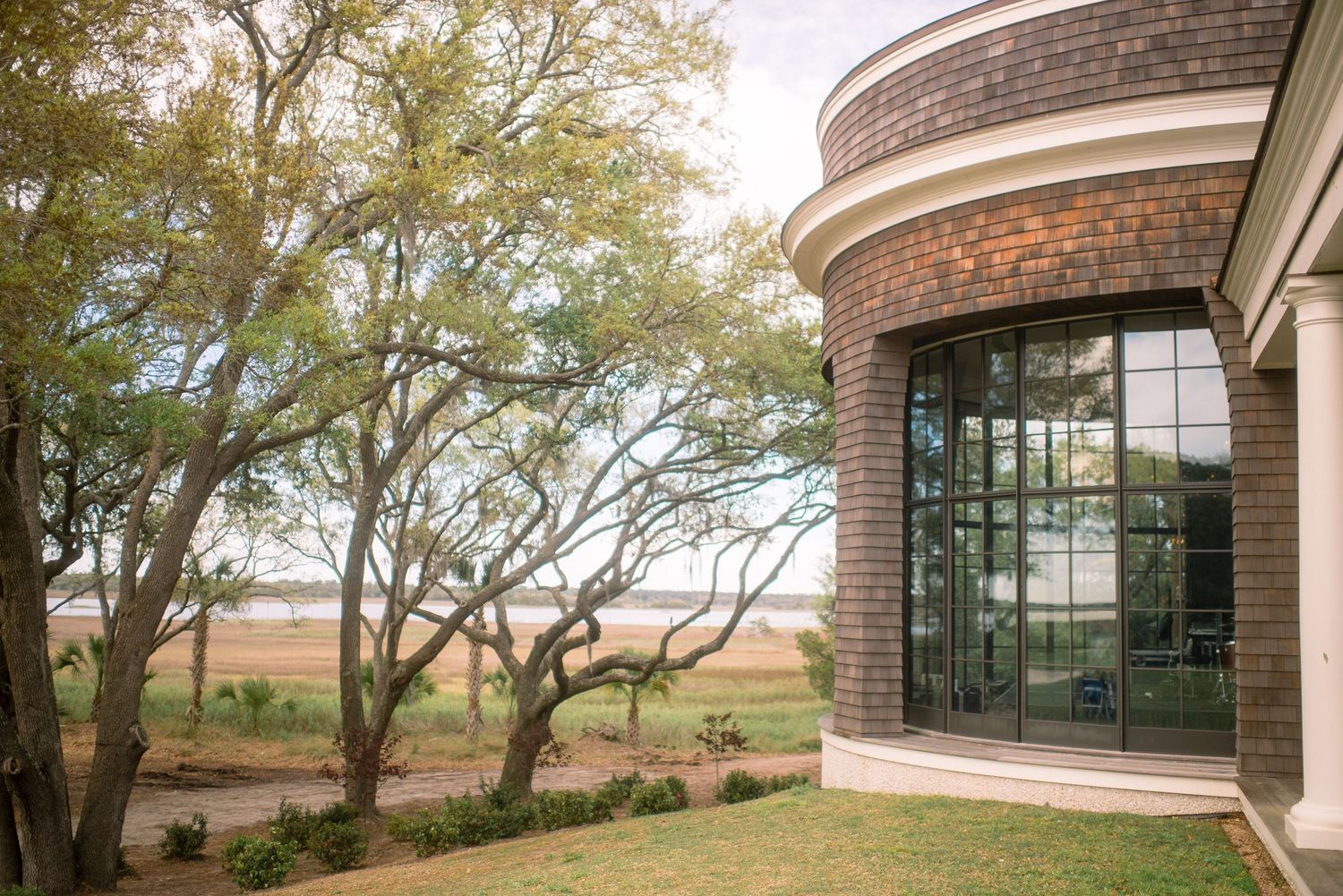 Modern brick building with curved glass windows sits nestled among mature trees on a rolling hillside landscape.