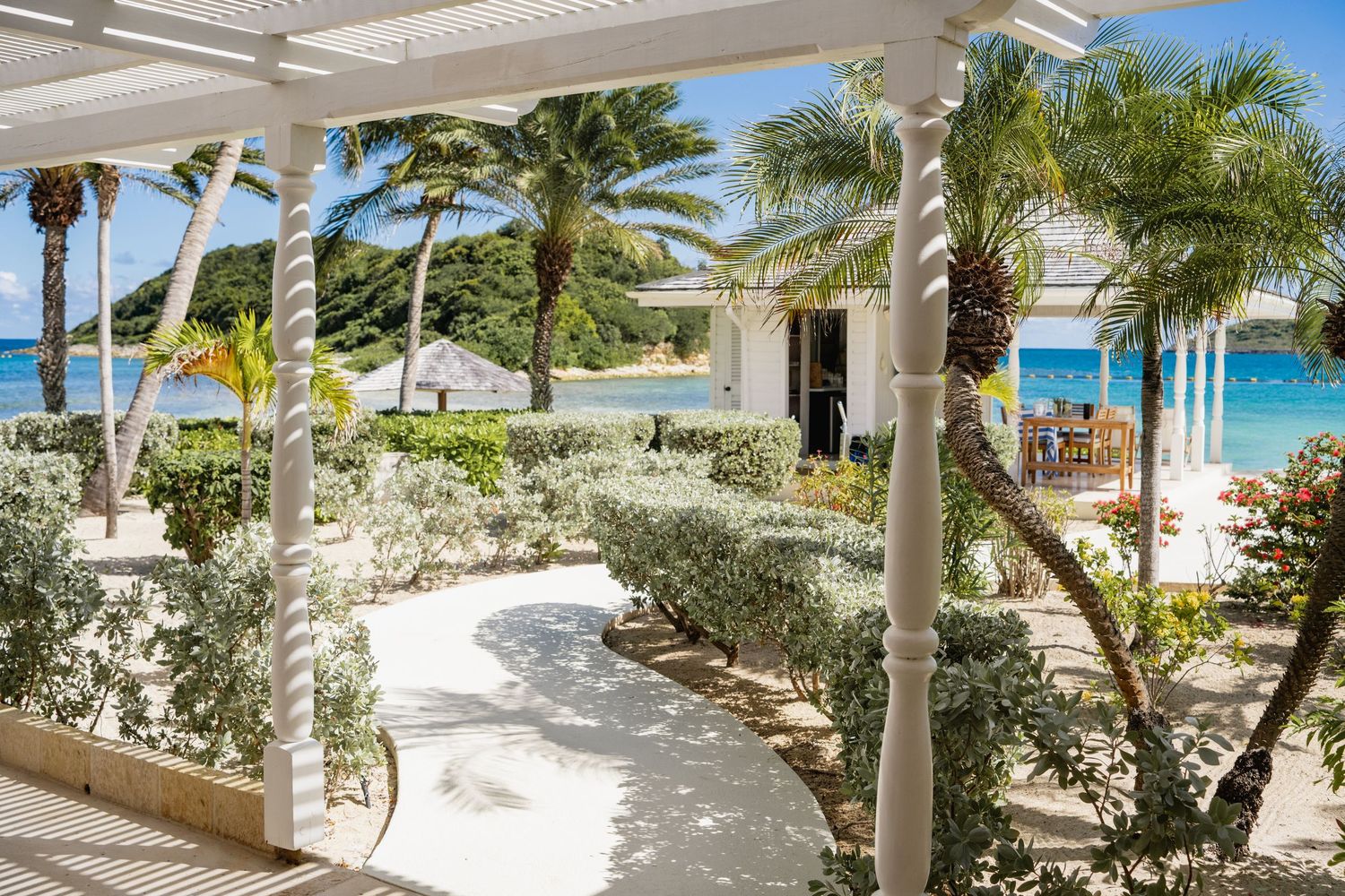 Palm trees line a winding stone pathway leading to a pristine tropical beach with turquoise waters.