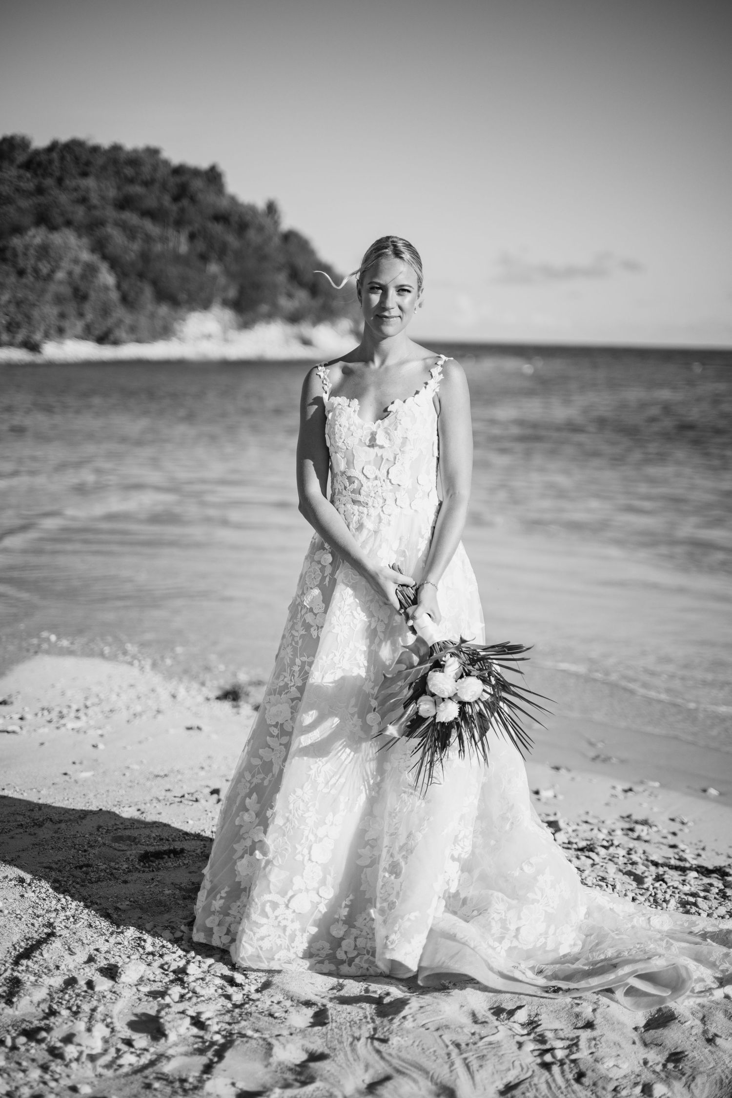 Black and white photos of bride in lace dress posing on a beach with bouquet.