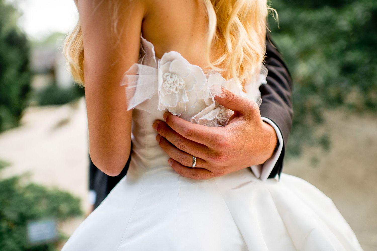 Elegant bride in white lace gown poses in outdoor garden setting during wedding photo session.