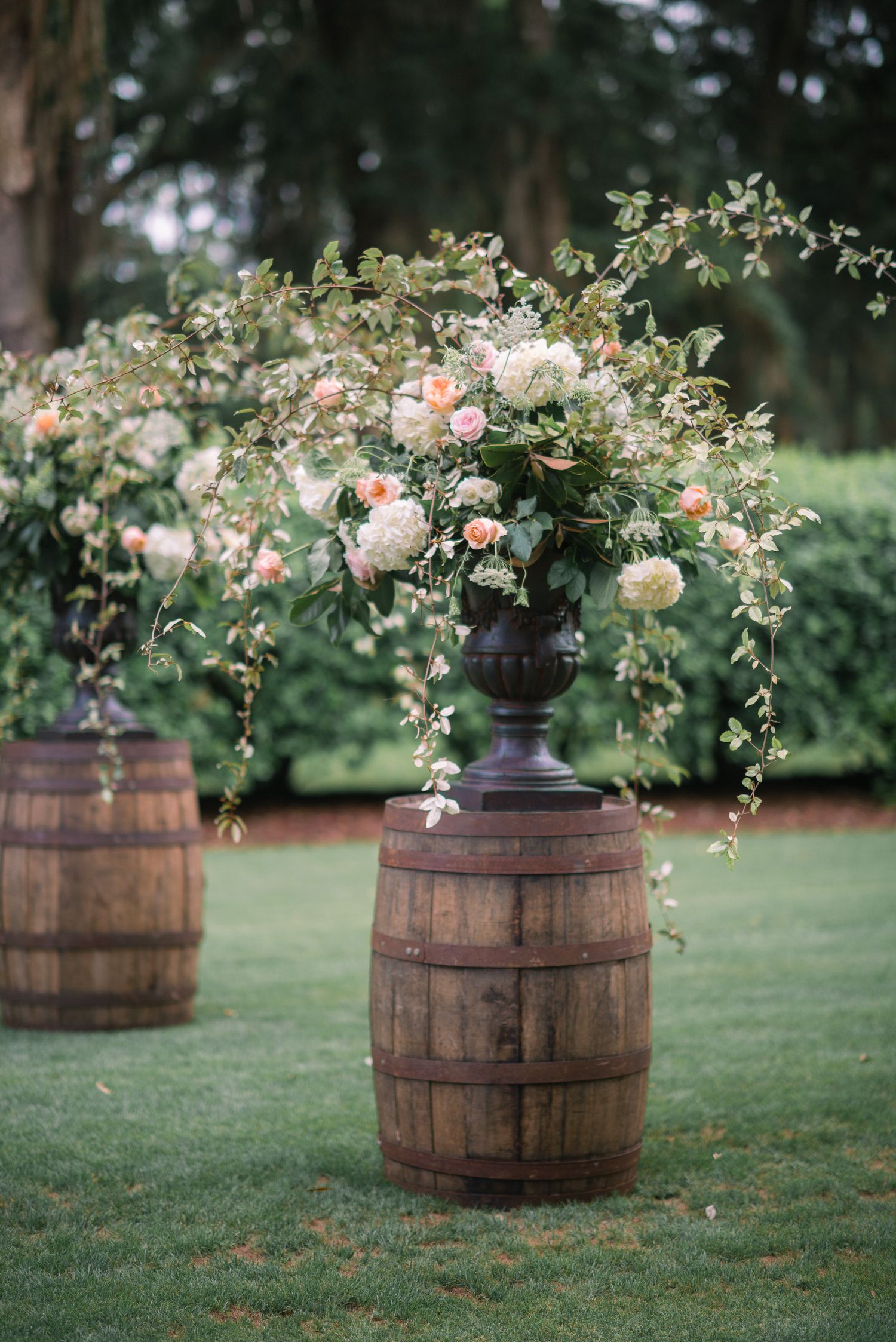 Rustic wooden wine barrels adorned with elegant floral arrangements create a charming outdoor wedding display.