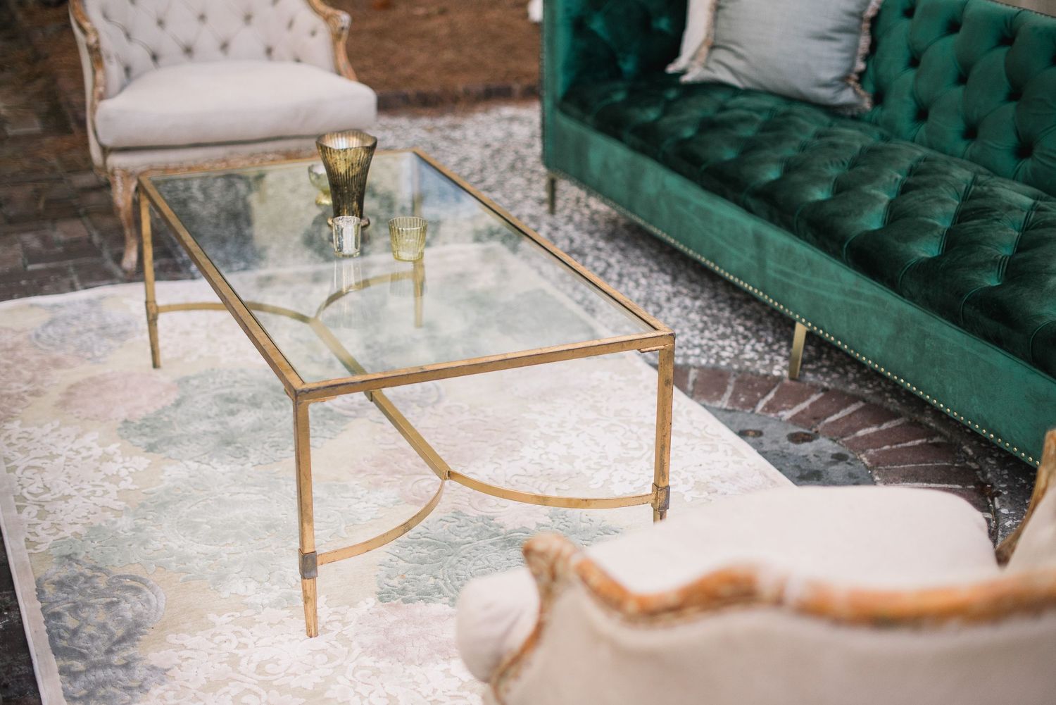 Emerald green tufted velvet sofa with gold metal frame sits elegantly against a textured wall.