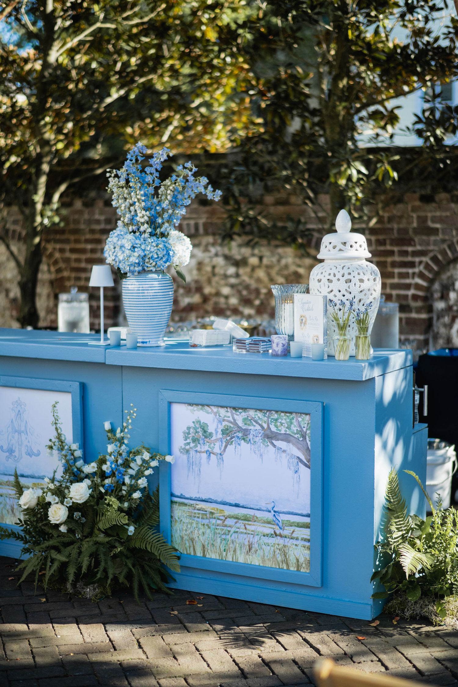 Light blue decorative planter boxes with white lanterns and floral arrangements create an elegant garden display.