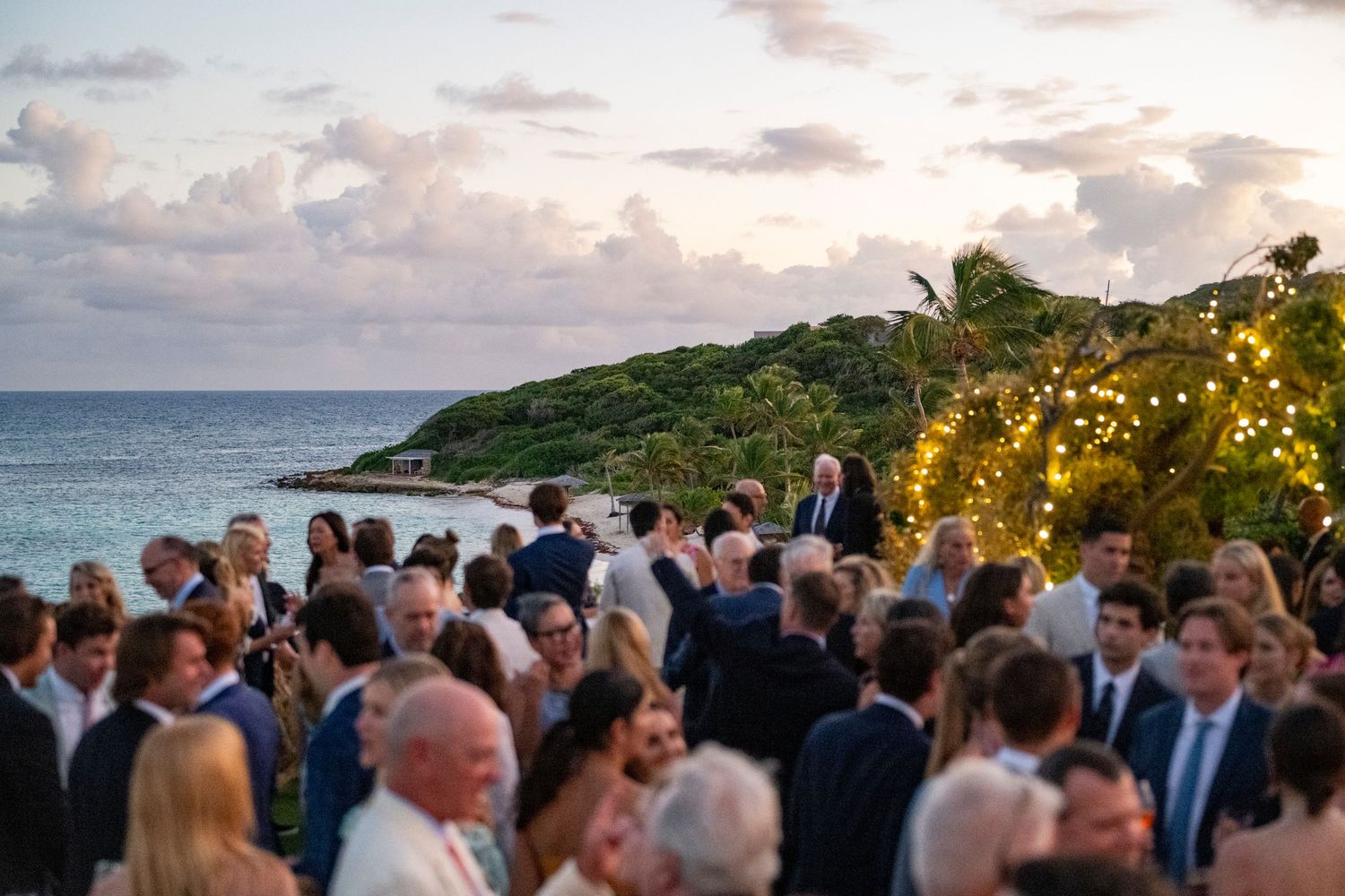 Crowd of wedding guests gathered at sunset overlooking an ocean view.