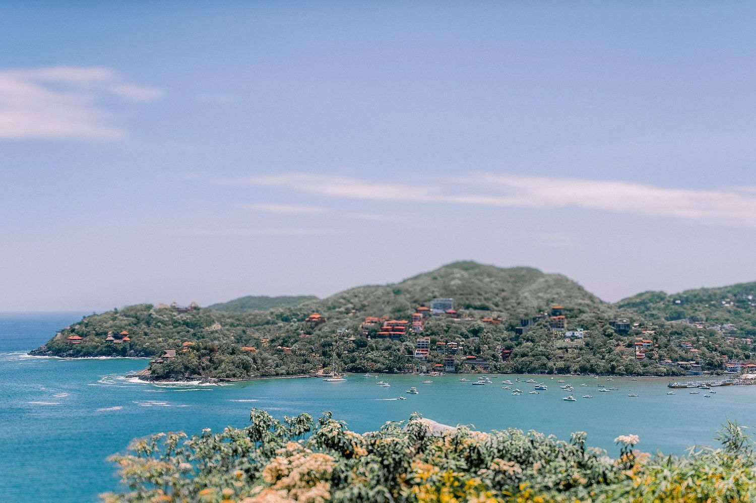 Aerial view of a Zihuatanejo, MX with lush green hills surrounding crystal blue waters.