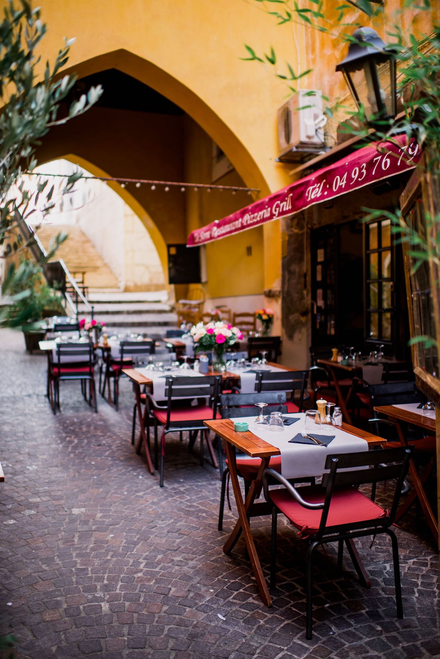 Charming outdoor restaurant seating area with red cushions under stone archways and cobblestone flooring.