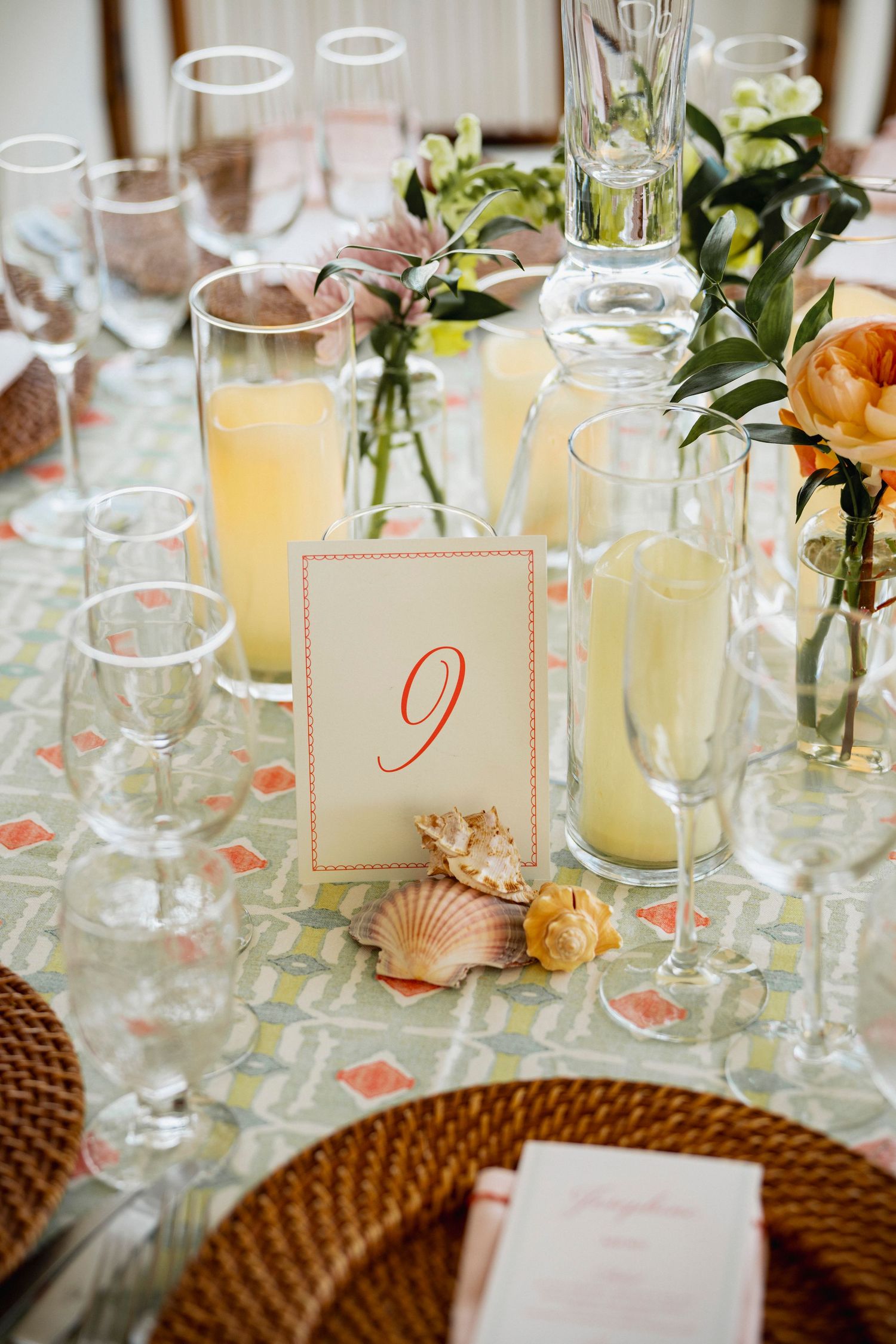 Elegant table setting with orange floral centerpieces, woven chargers, and citrus cocktails in crystal glassware.