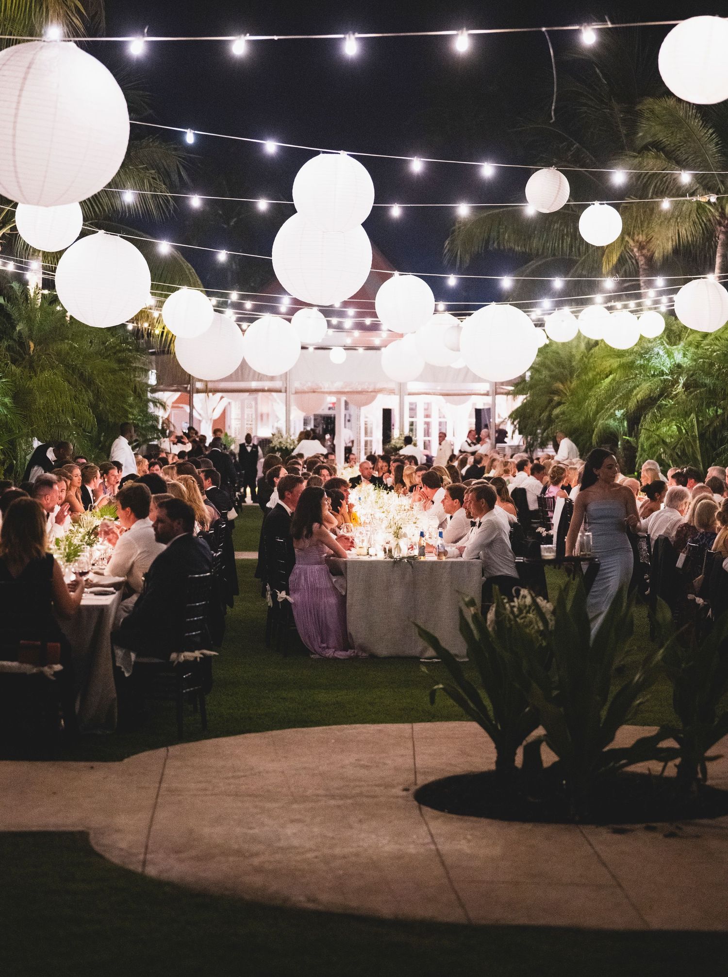 Outdoor wedding reception at night with white paper lanterns and string lights creating a romantic ambiance.