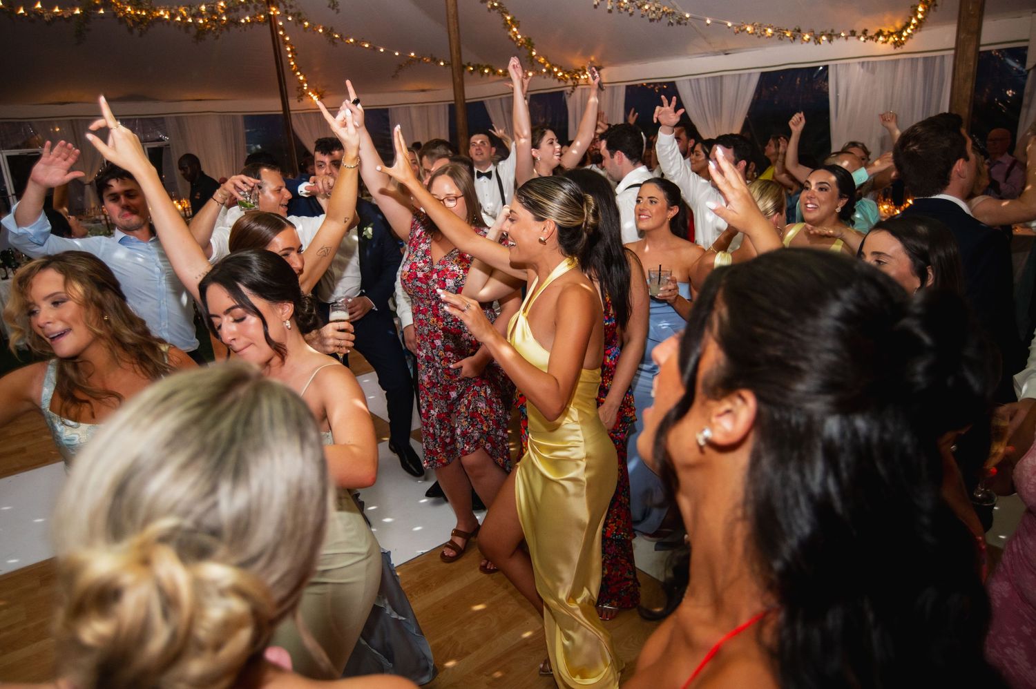 Wedding reception dance floor filled with guests dancing under string lights.