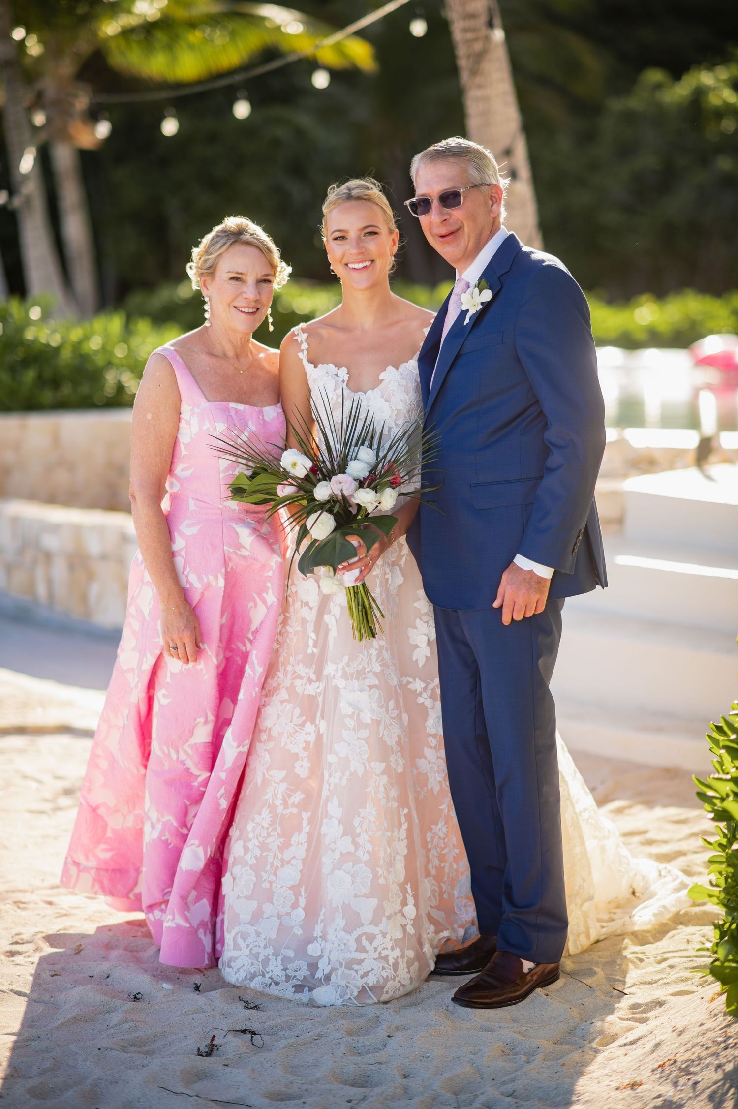 Wedding party poses together on beach path in pink and white dresses and blue suit.