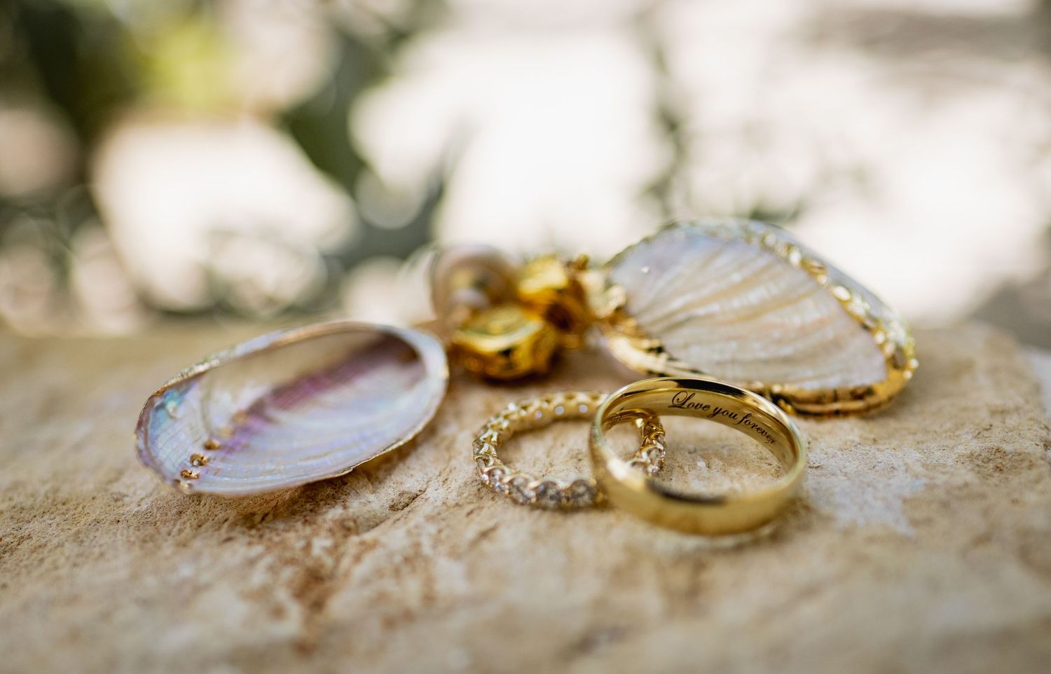 Wedding rings and seashells arranged artistically on sandy beach background.