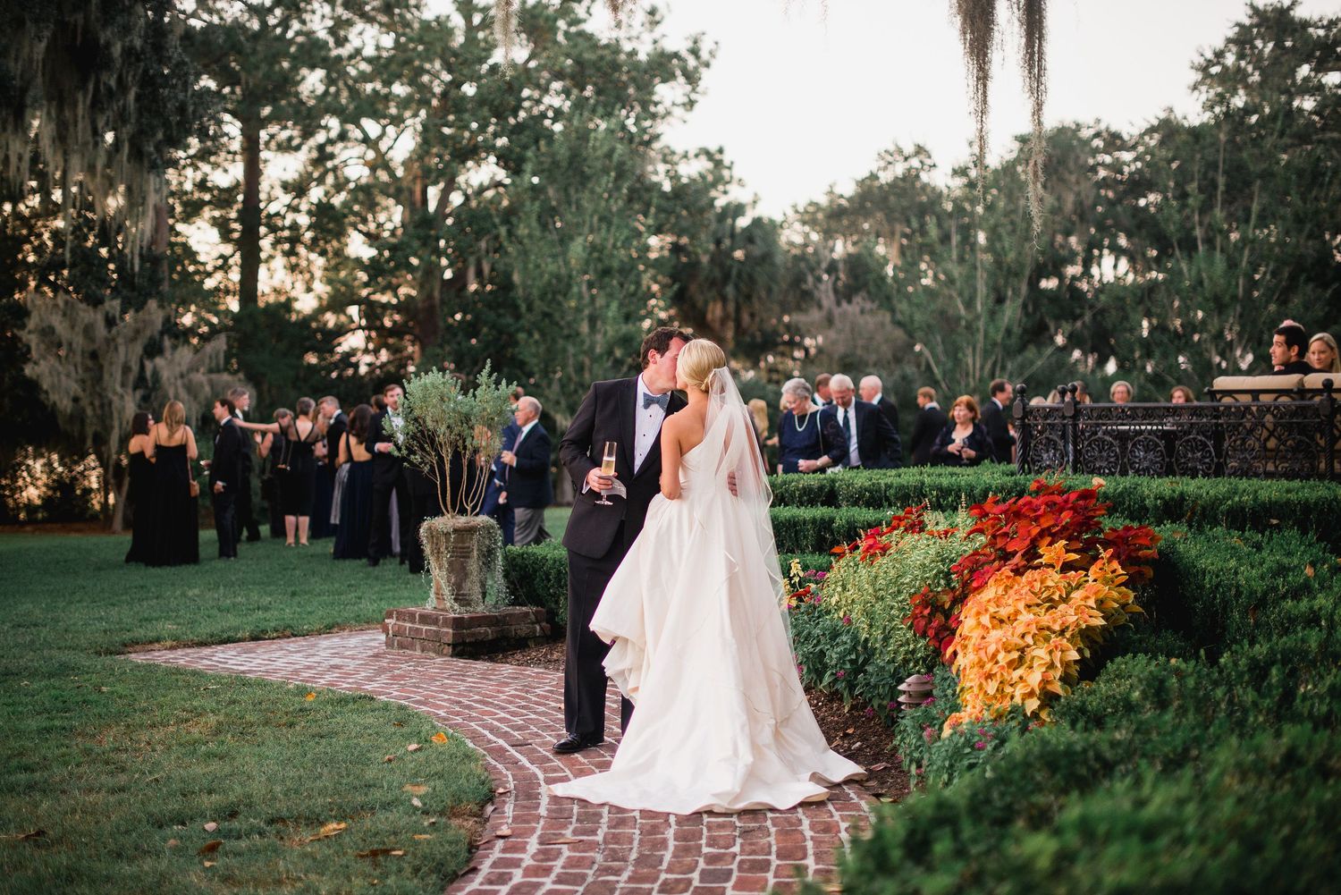 A romantic outdoor wedding ceremony set in a lush garden with Spanish moss draped trees and vibrant fall floral arrangements.