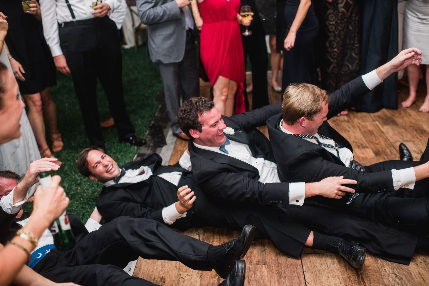 Wedding guests in formal attire lay on a wooden dance floor during a fun reception moment.